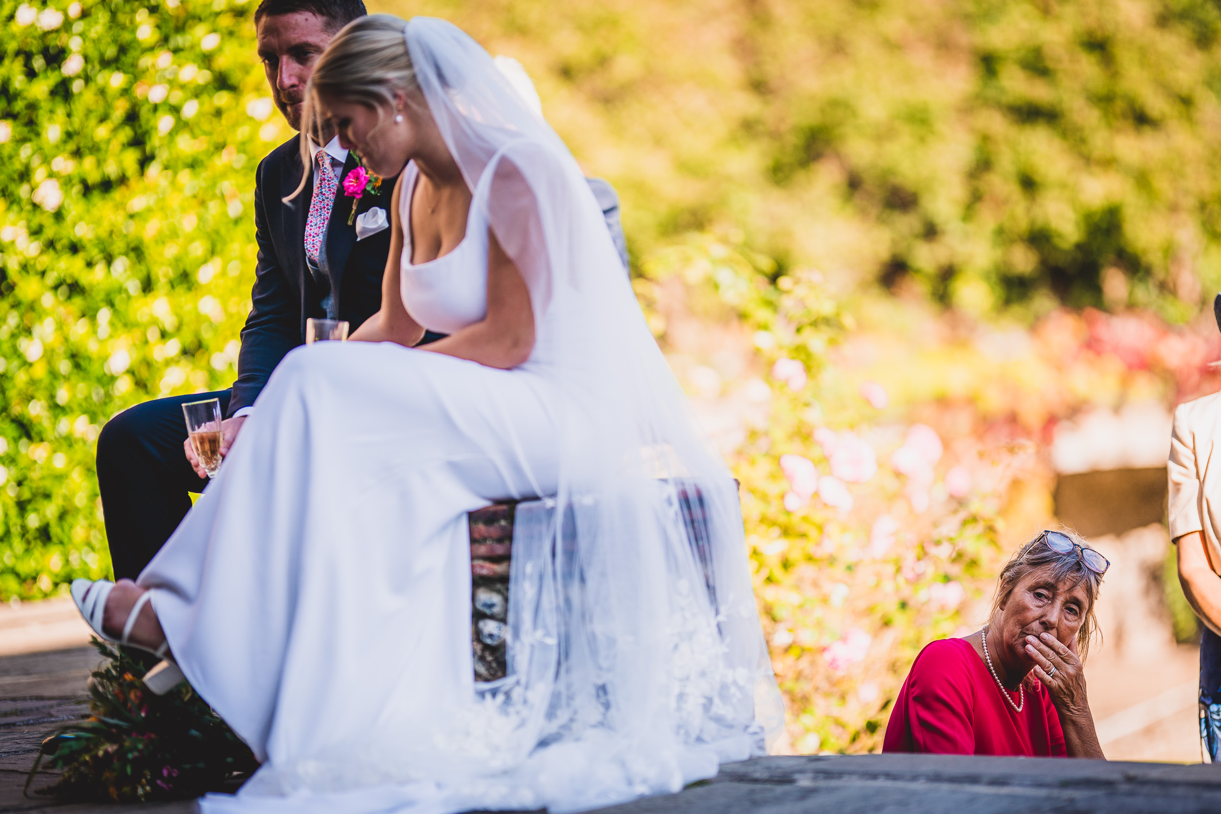 A groom and bride posing for their wedding photo on a garden bench.