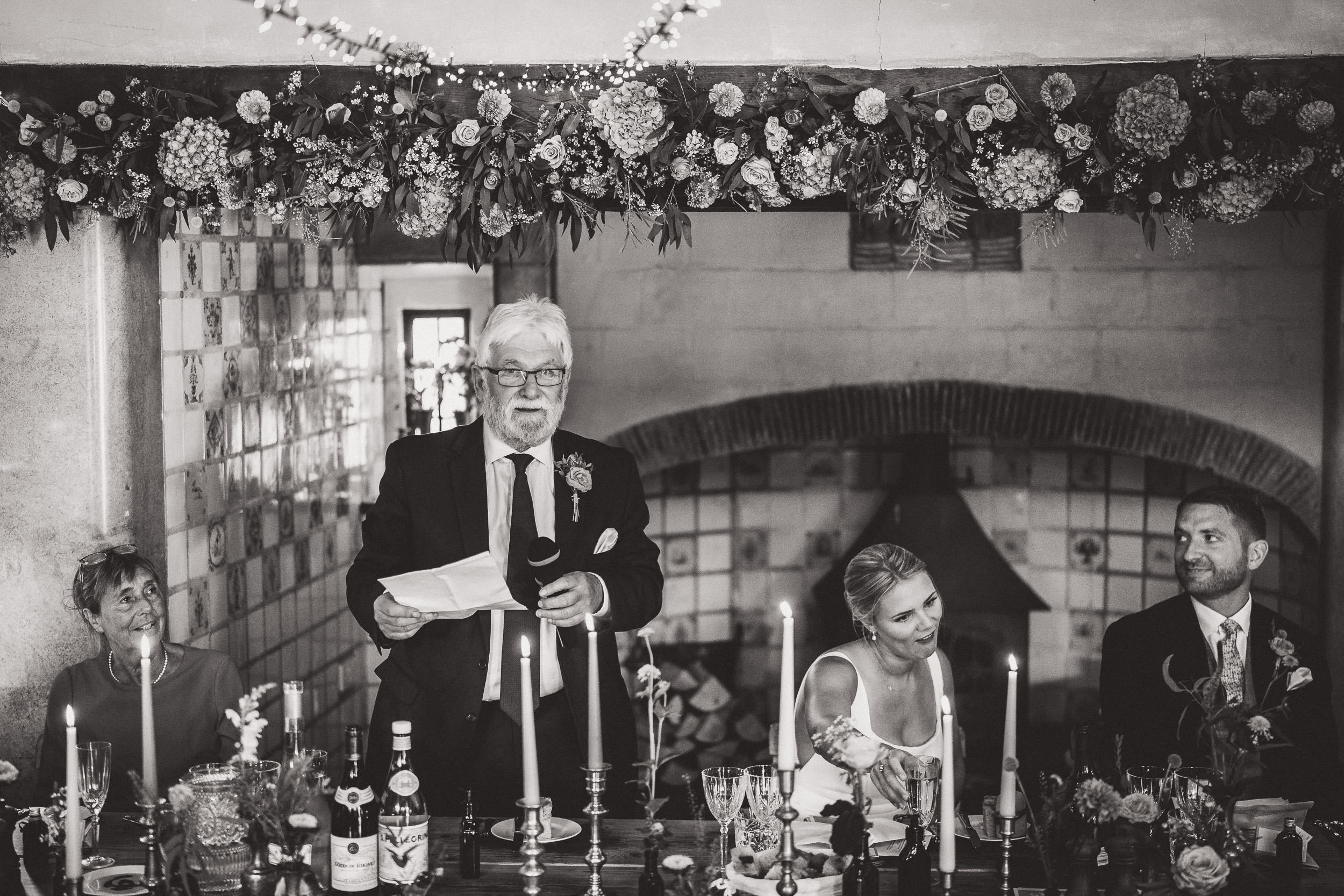 A black and white wedding photo of a man giving a speech.