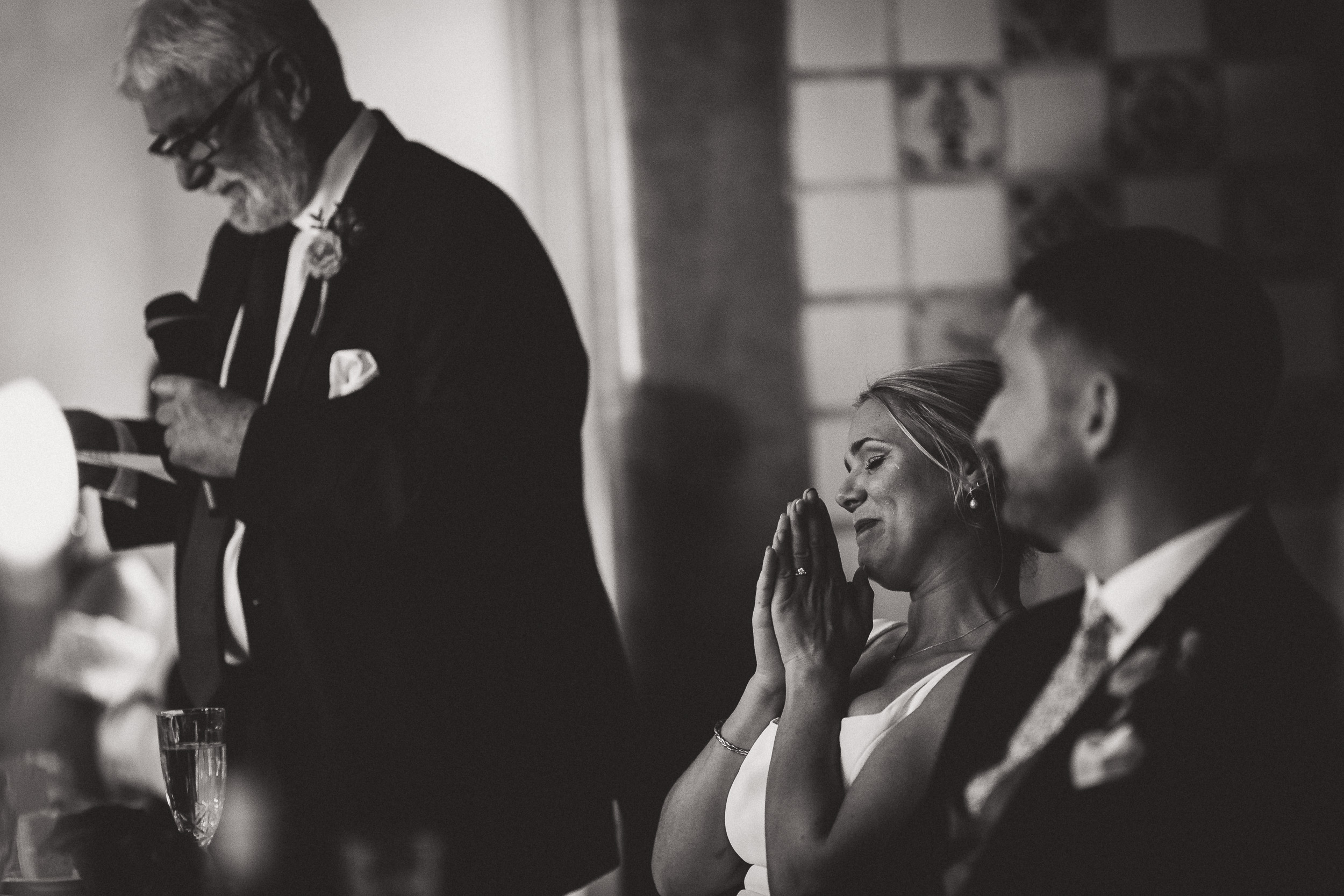 A wedding photographer captures the joyful bride and groom clapping during their speech.