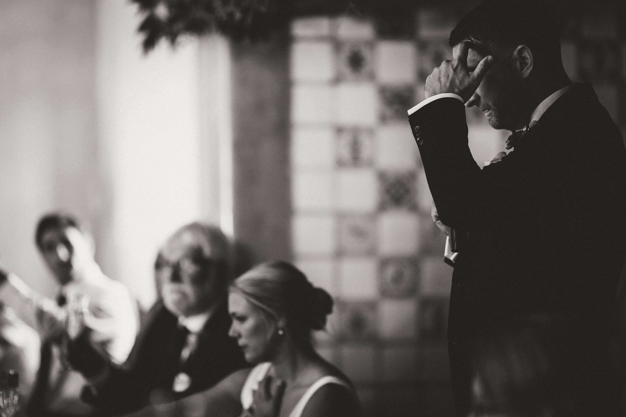 A groom in a classic tuxedo is giving a heartwarming speech at his elegant wedding.