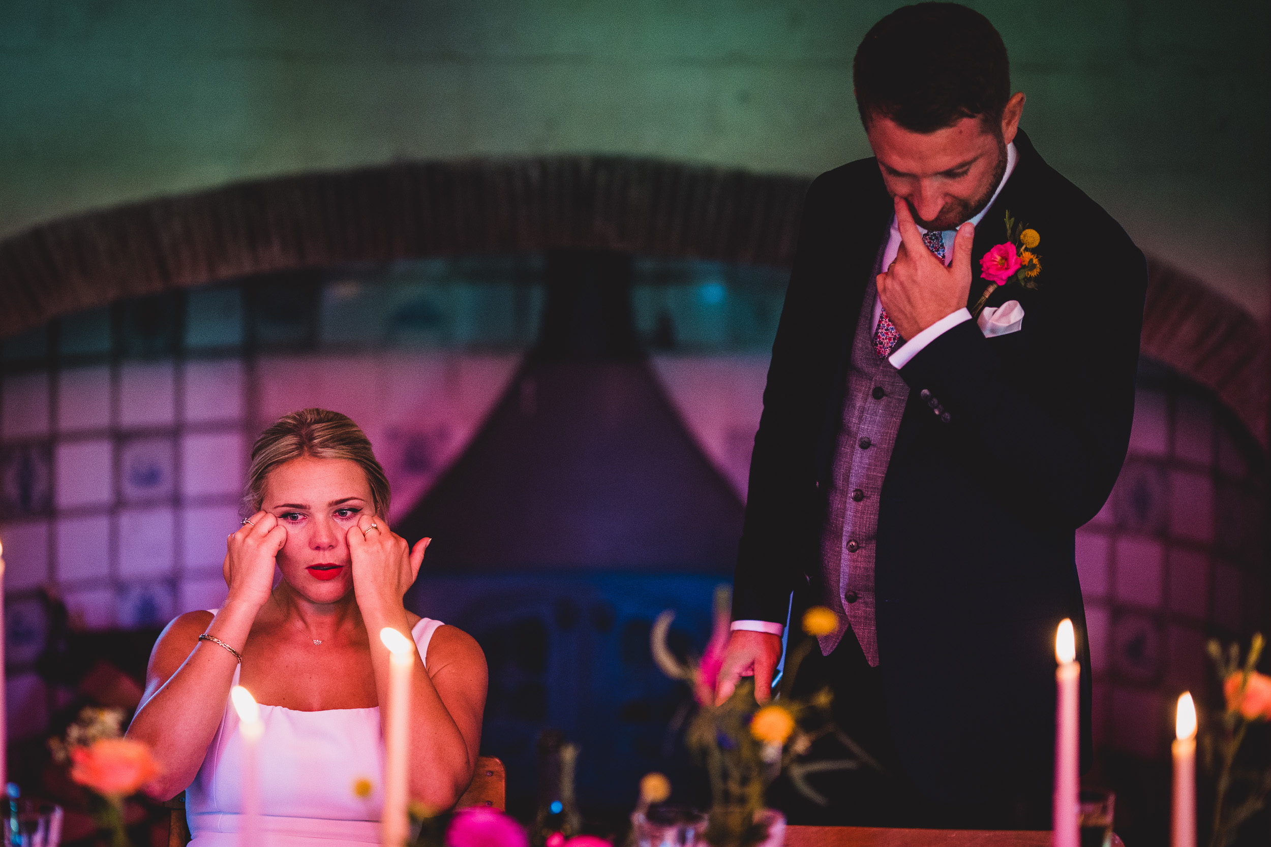 A bride and groom pose at their wedding table, captured by a wedding photographer amidst flickering candles.