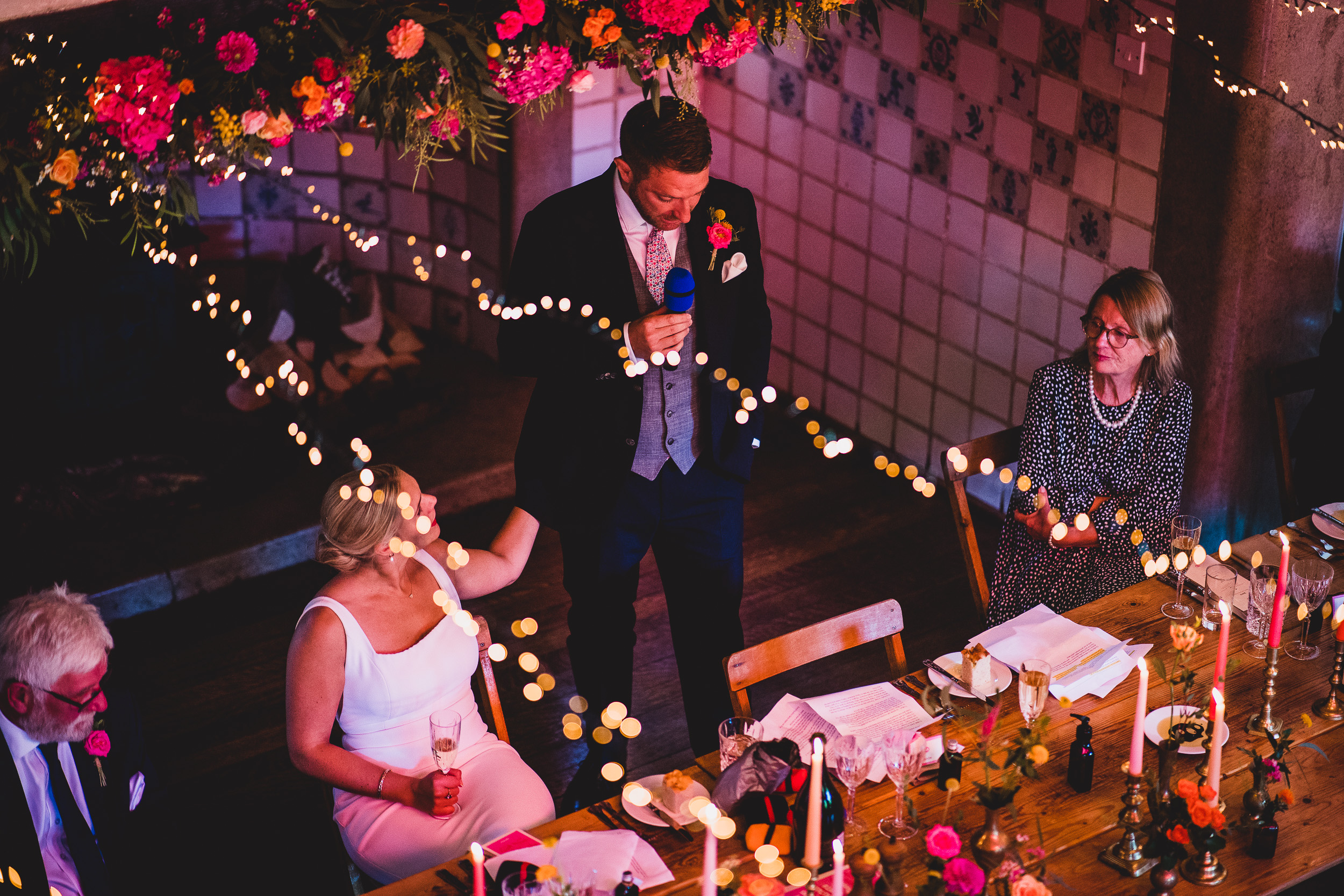 A wedding photographer captures a lovely bride and groom surrounded by flowers at a beautifully decorated table.