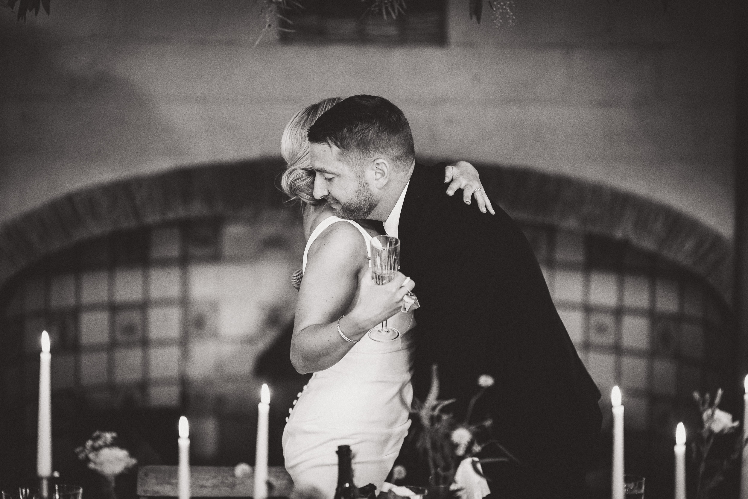 A groom hugging his bride, captured by a wedding photographer amidst a candlelit setting.