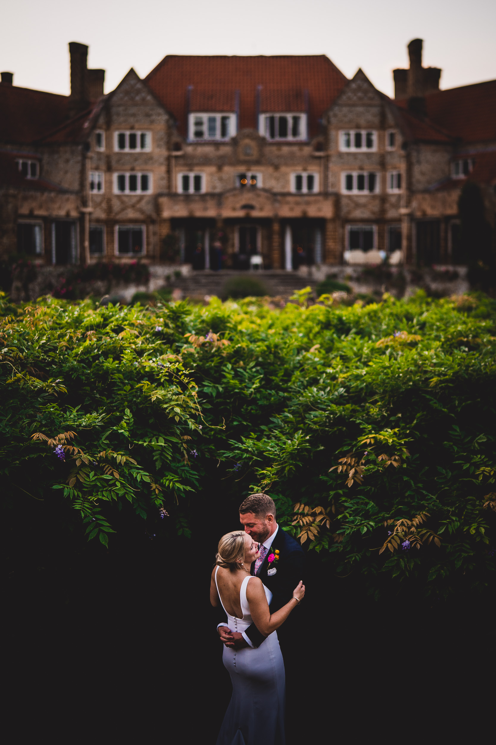 A wedding couple embracing in front of a mansion.