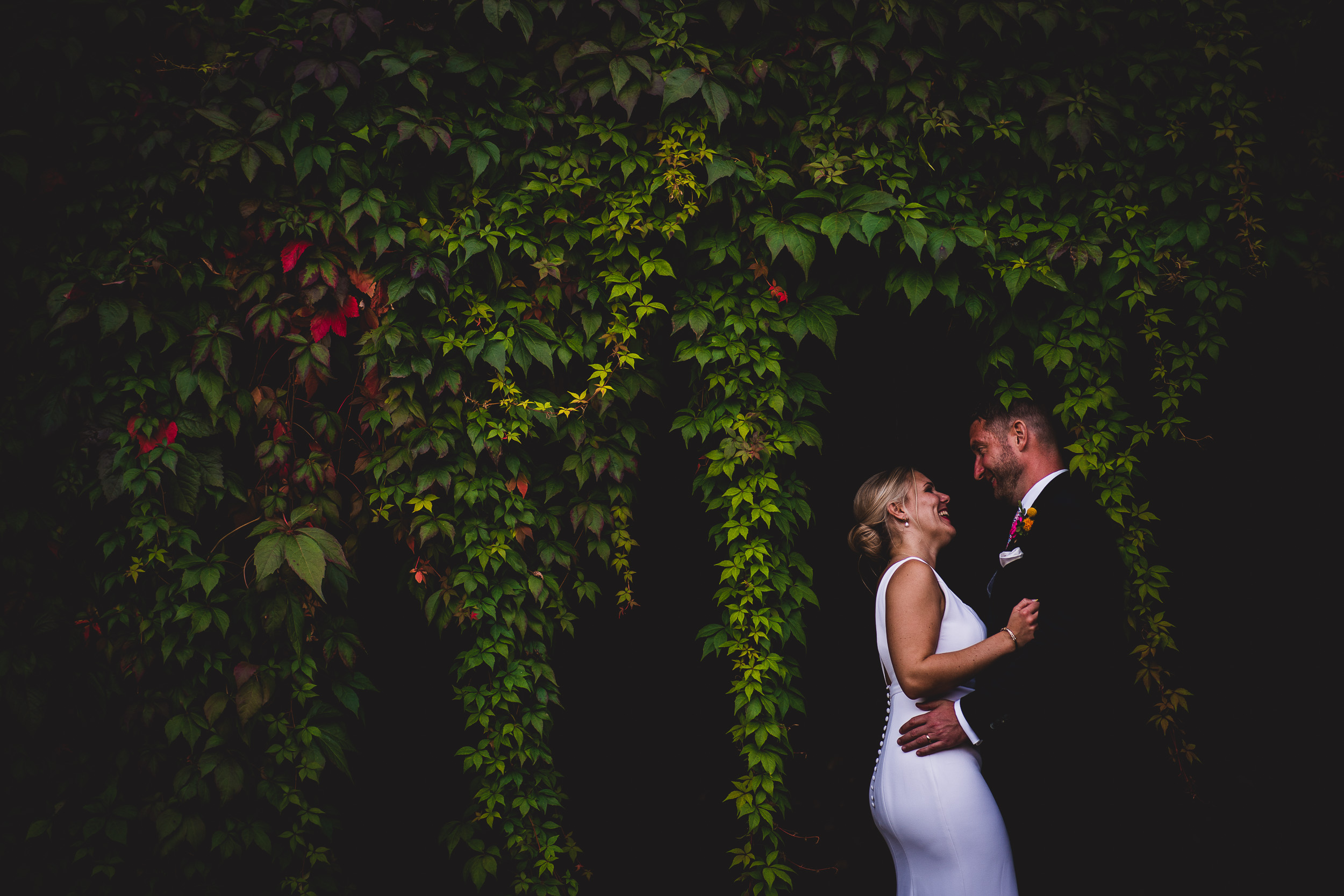 A wedding photo capturing a bride and groom amidst ivy covered walls.