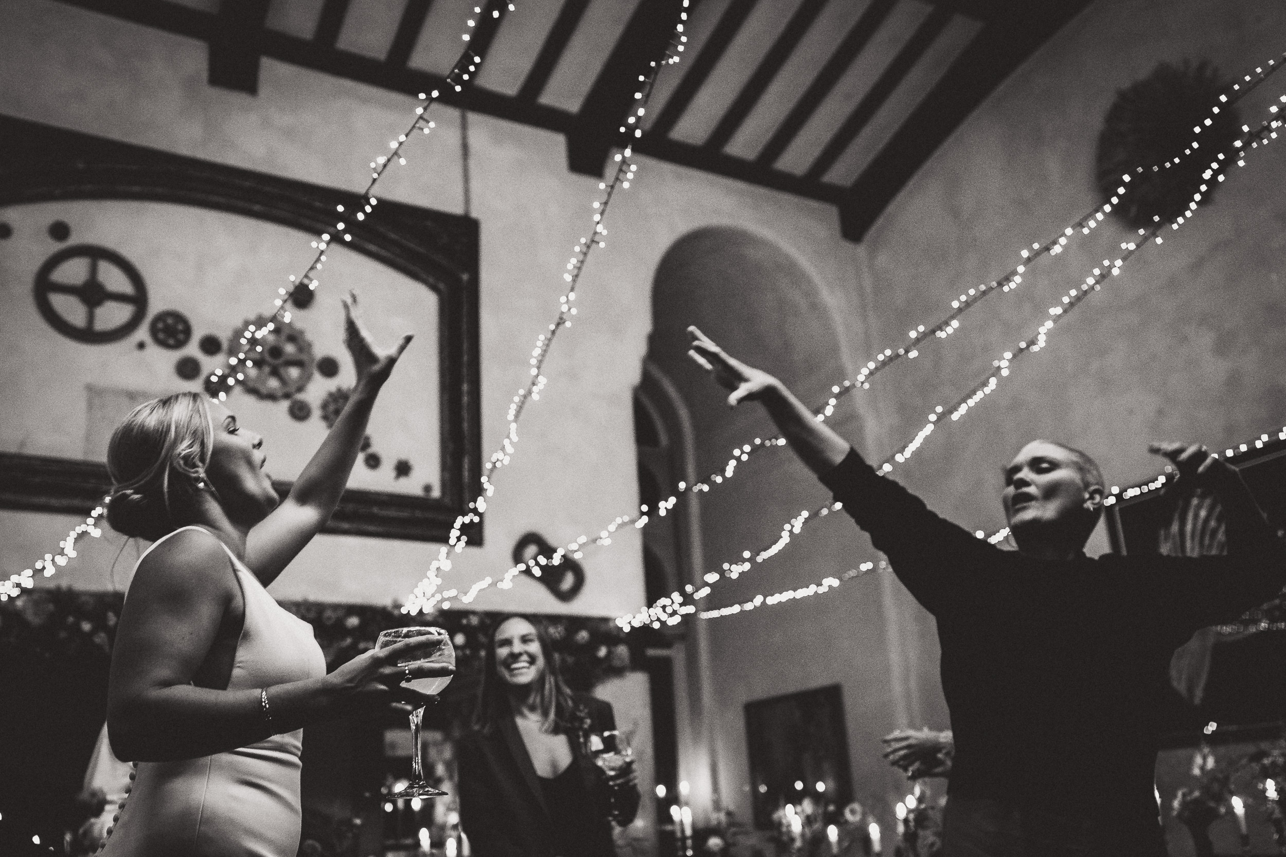 A groom and his wedding photographer capture a group of people dancing in a room with lights.