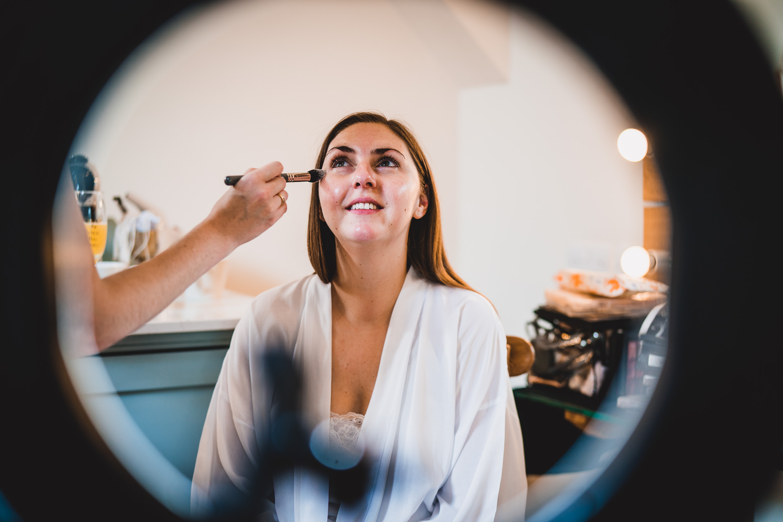 A bride having her makeup done in front of a mirror, captured by the wedding photographer for a stunning wedding photo.