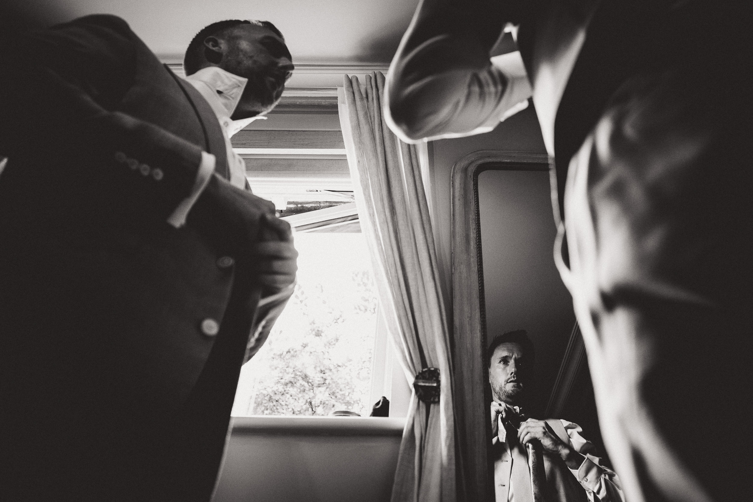 A groom is preparing in front of a mirror on his wedding day.