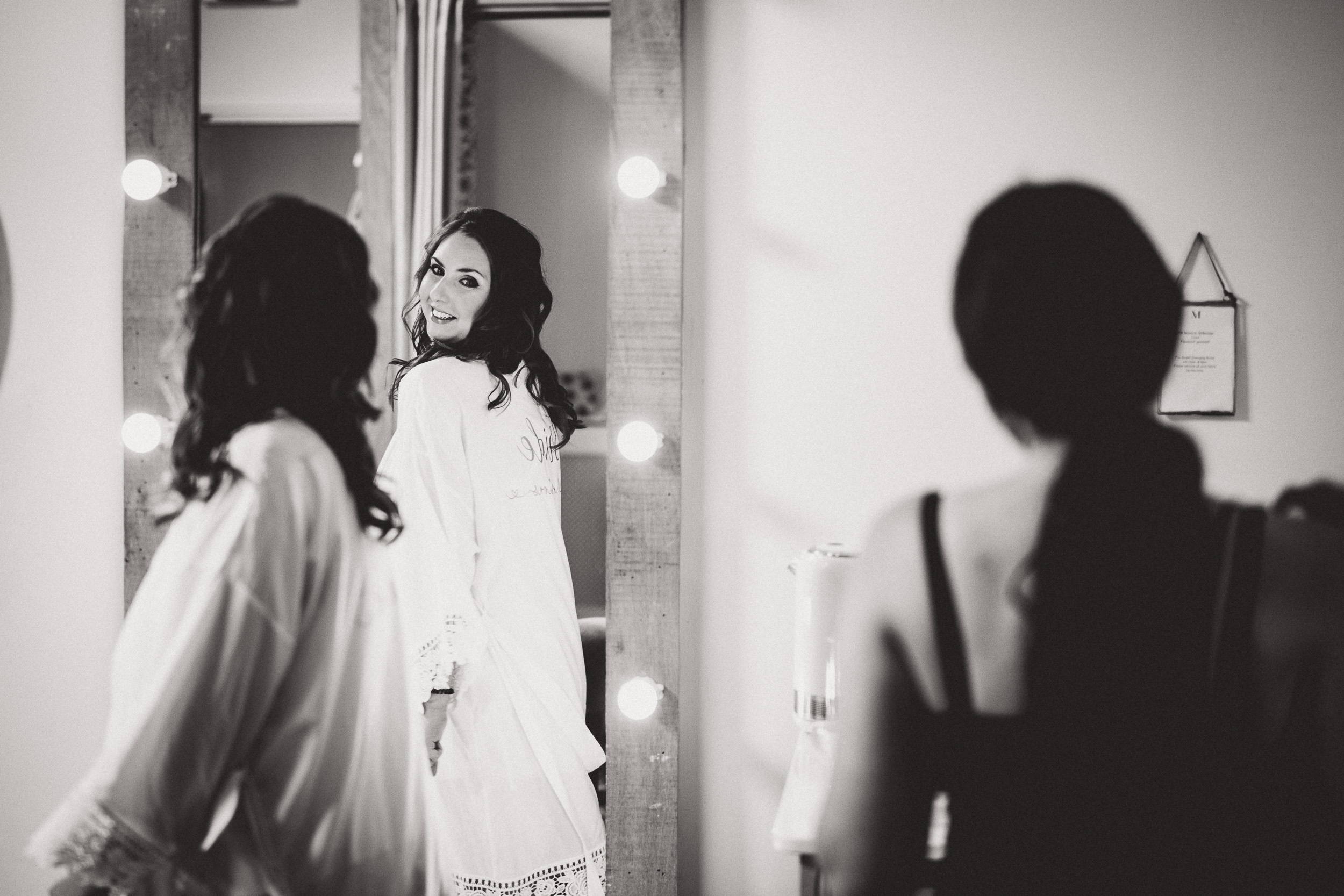 A bride in a robe admiring herself in the mirror on her wedding day.