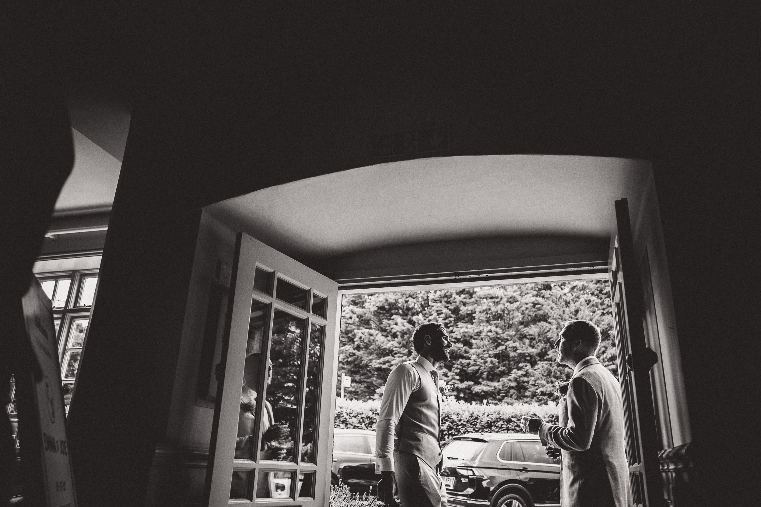 Two men in a wedding photo standing in the doorway of a house.