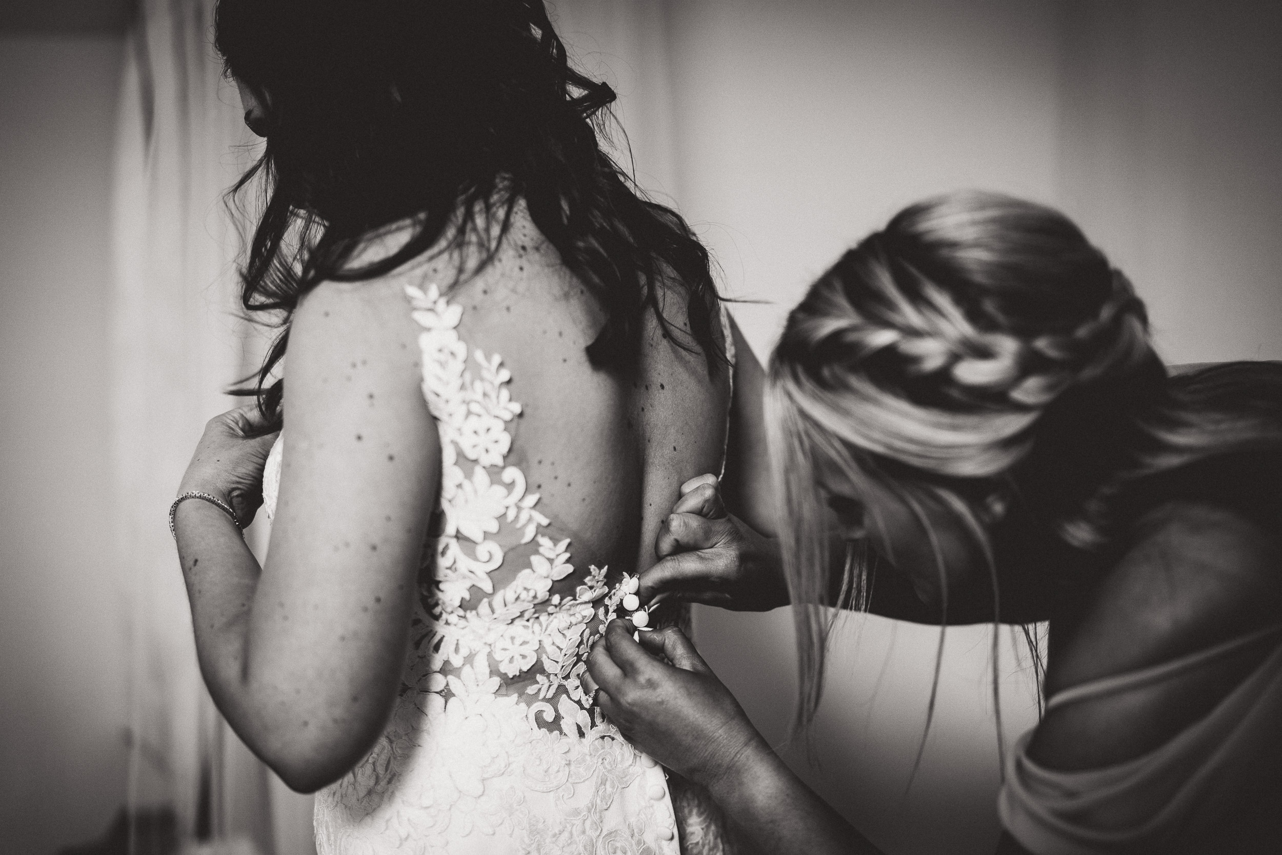 A bride and groom in a wedding photo, with the bride putting on her wedding dress.