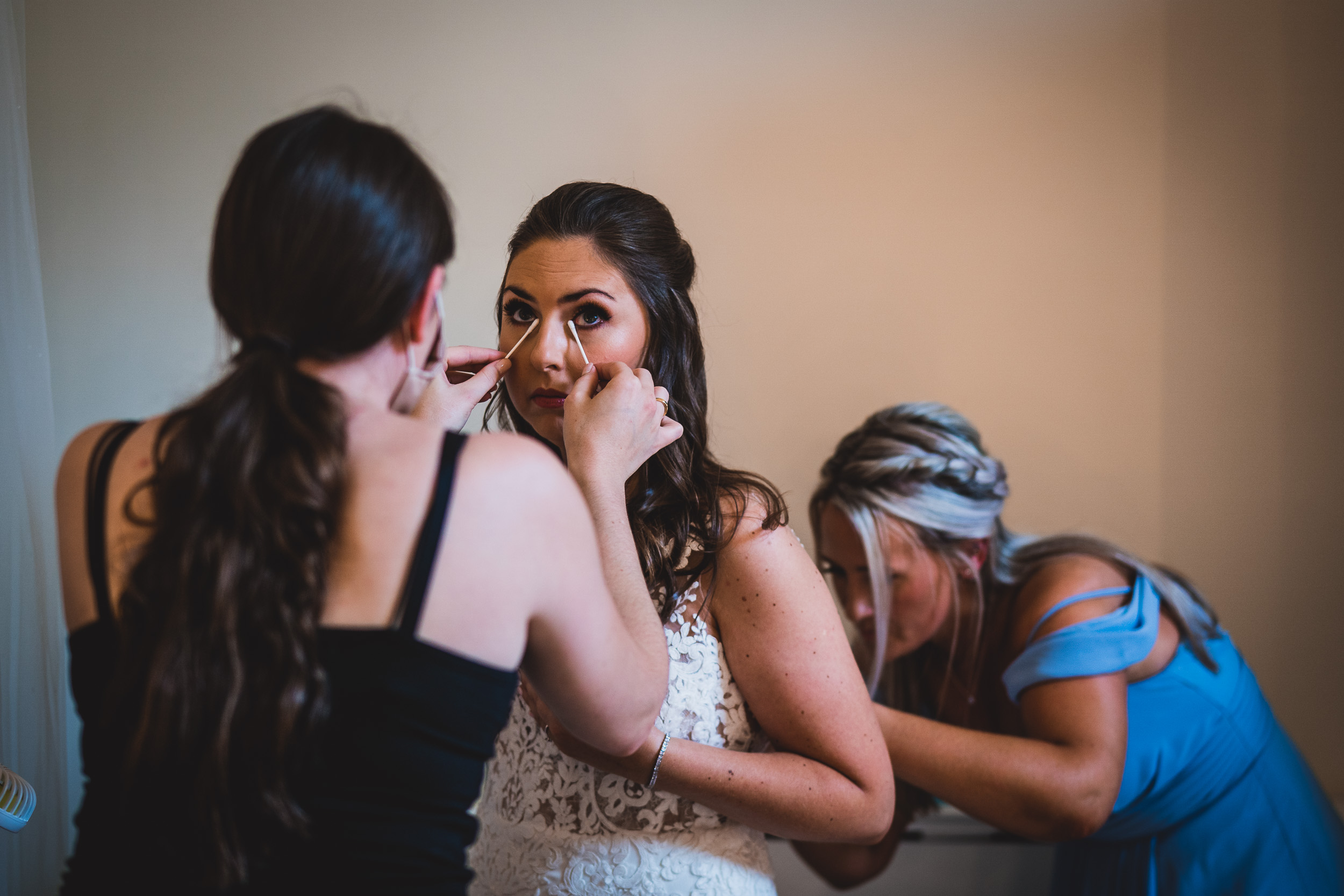 A bride getting her wedding makeup done by a bridesmaid.