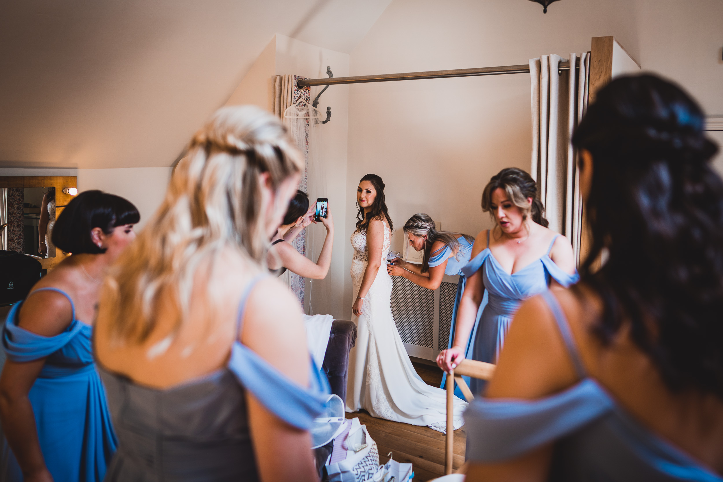 A bride is getting ready for her wedding with her bridesmaids and wedding photographer.