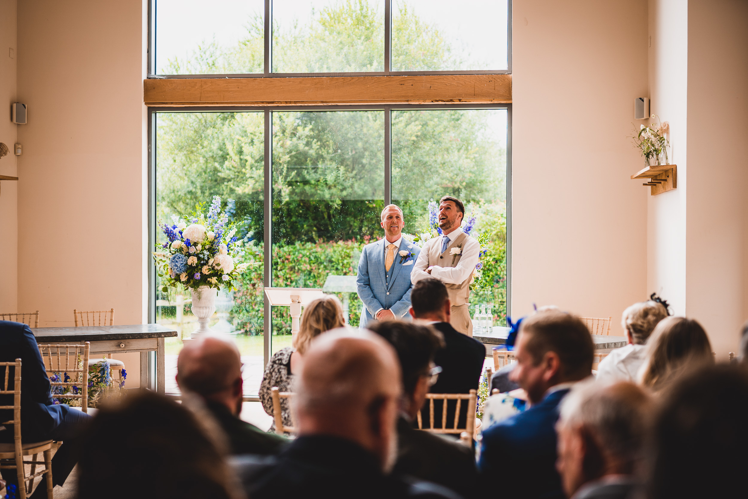 A wedding ceremony with a groom and bride in a room with large windows.