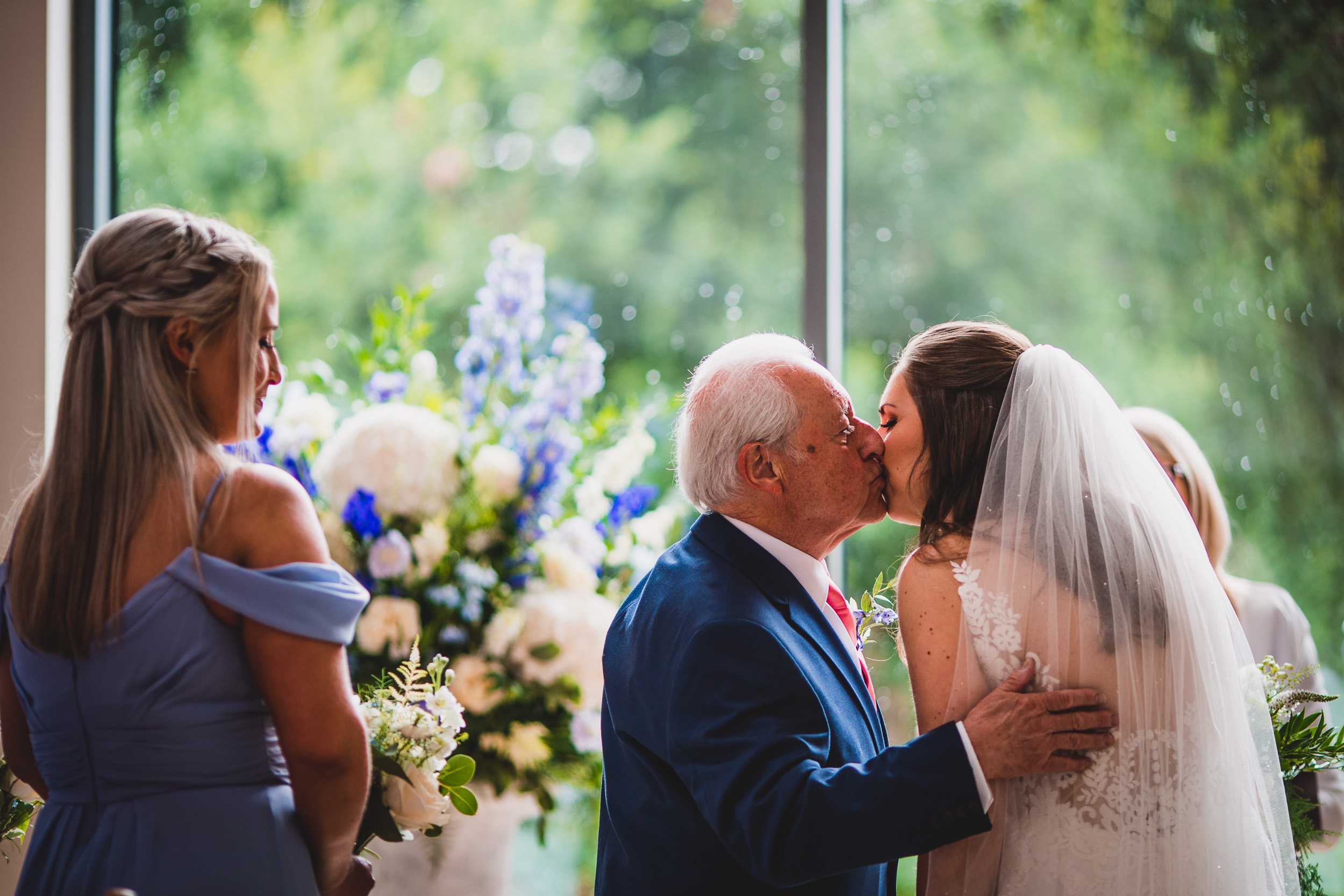 A bride kisses her father during a wedding ceremony captured by a wedding photographer.