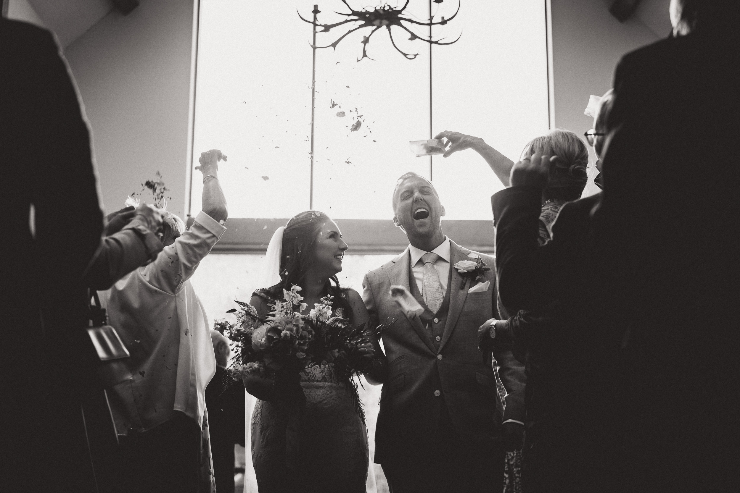 A black and white wedding photo of a bride and groom throwing confetti at each other.