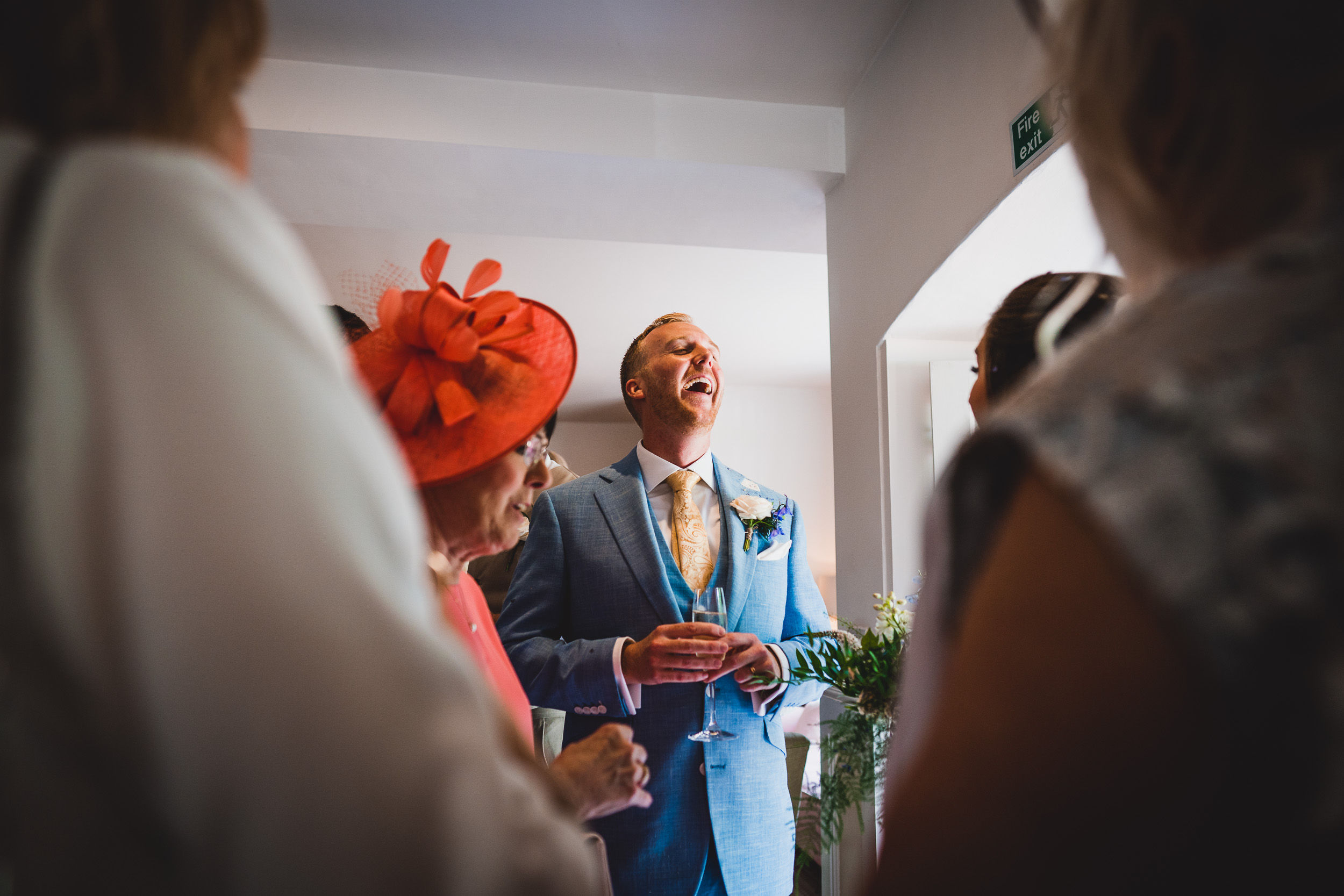 A groom in a blue suit is laughing in front of a group of people.