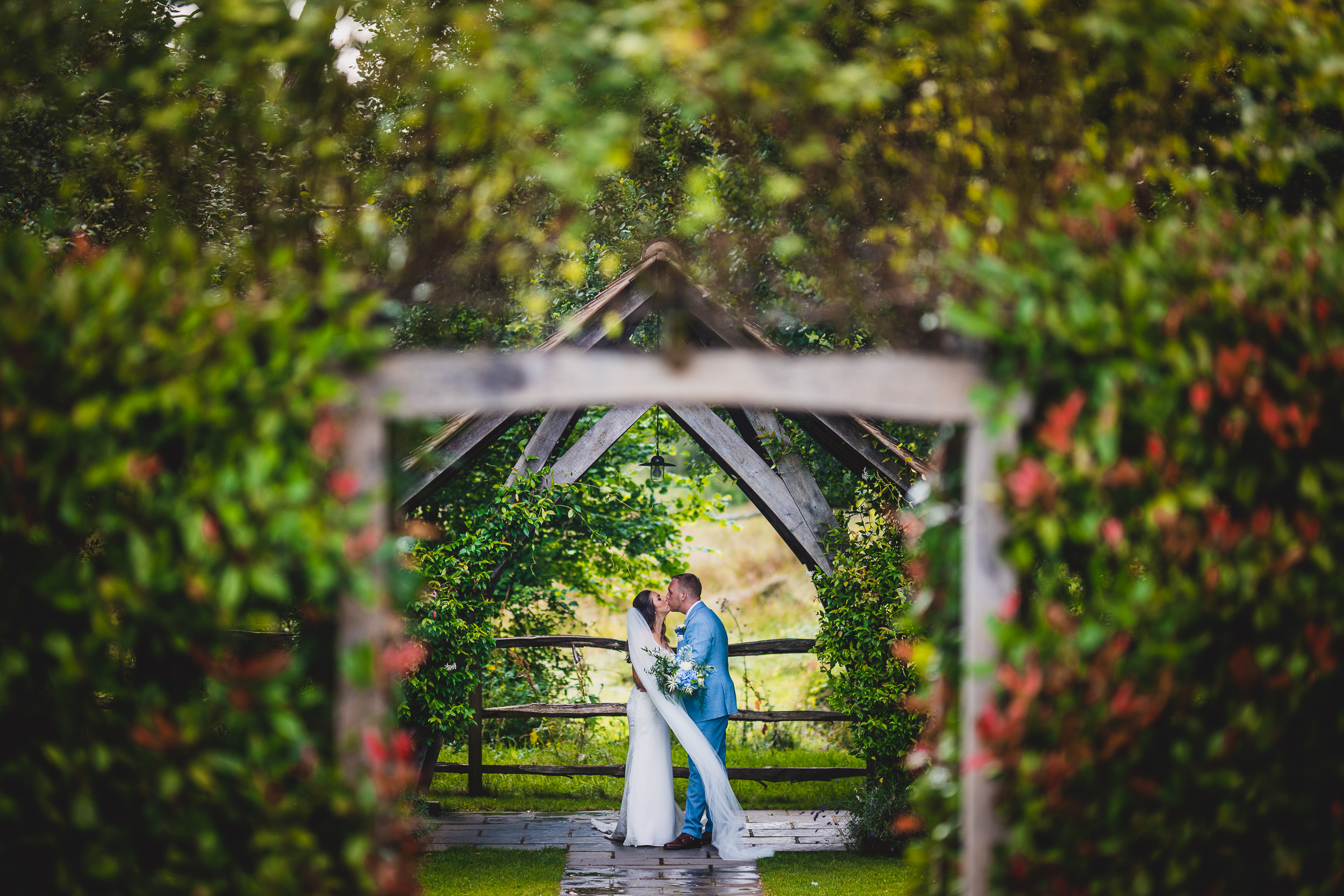 A wedding photographer captures a bride and groom kissing in a garden.