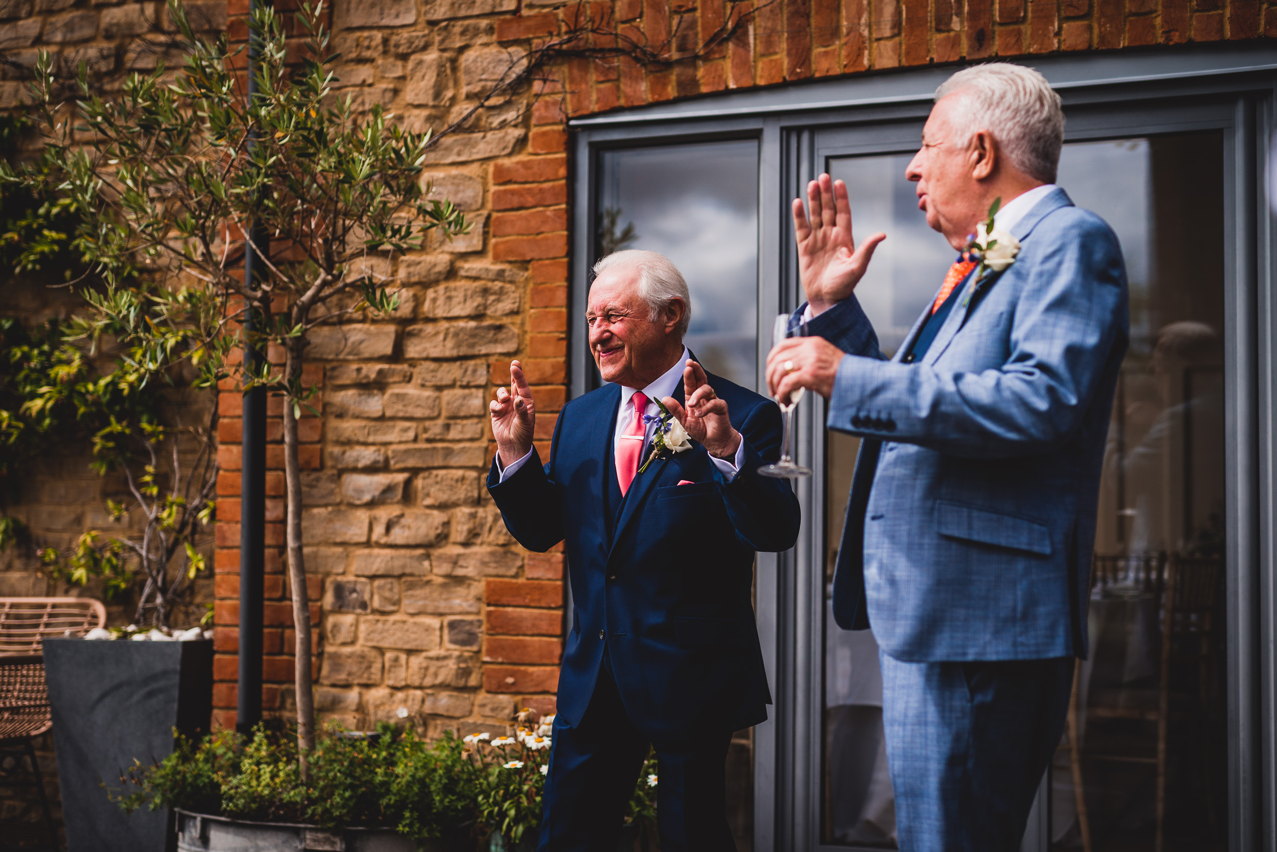 Two men in suits clapping at a wedding.