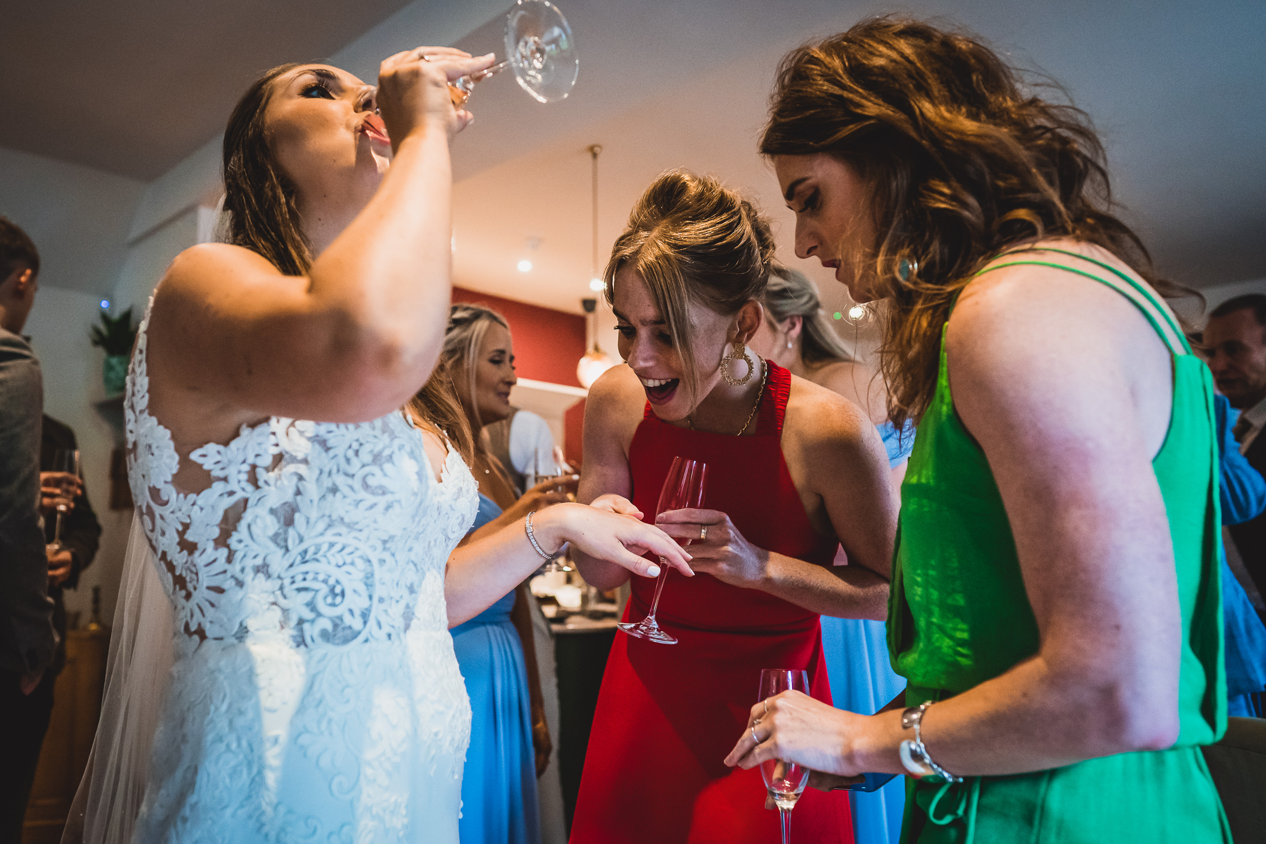 A wedding photographer captures the bride and bridesmaids enjoying wine at the reception.