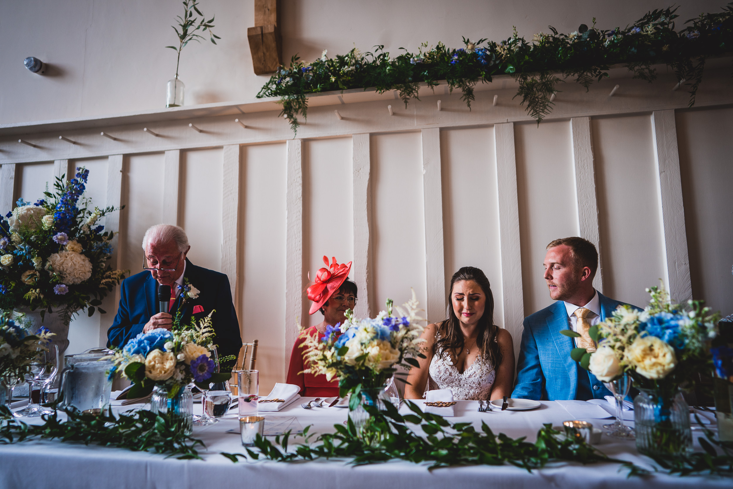 A wedding photographer capturing a bride and groom at a table with a bouquet of flowers.