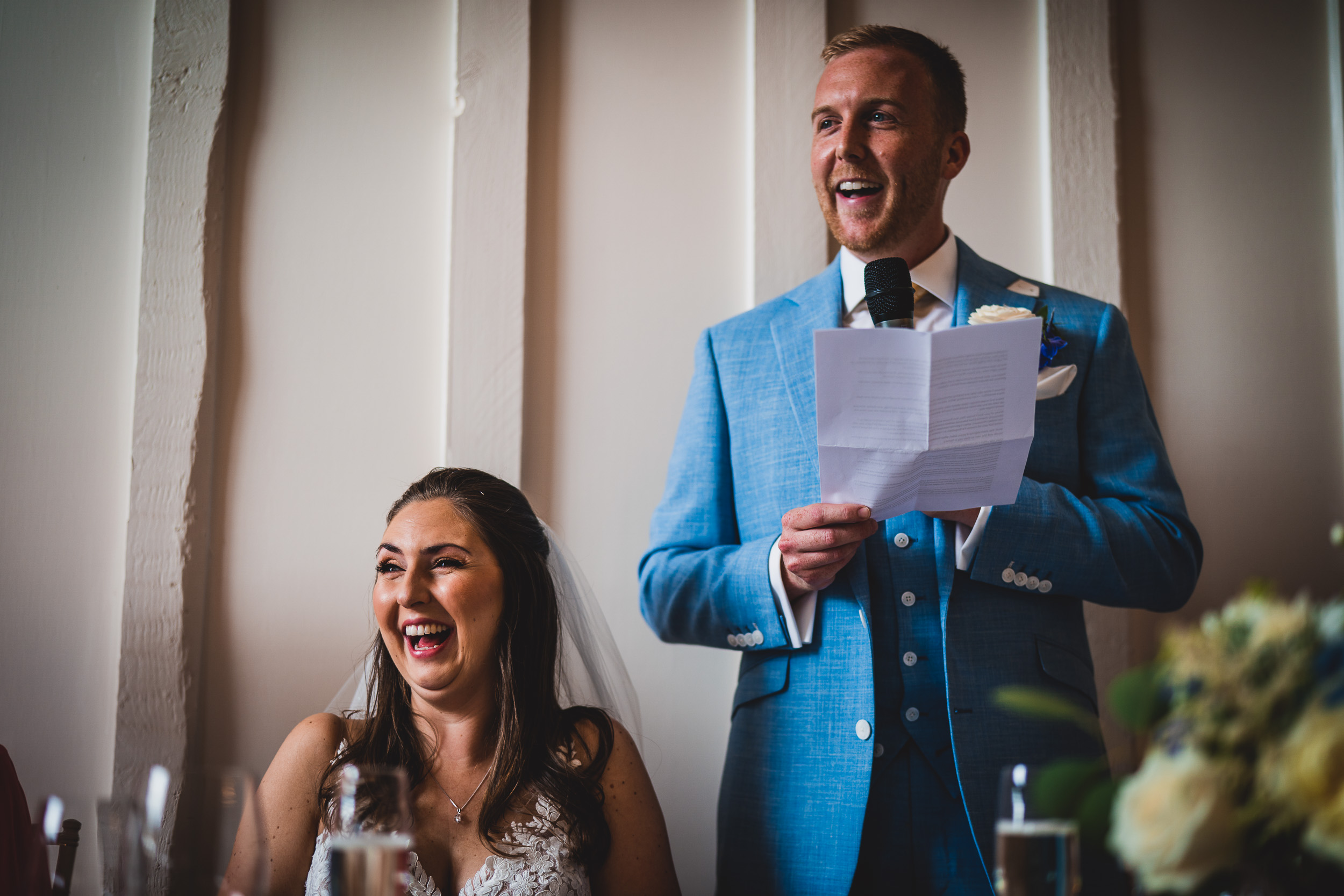 A groom and bride sharing laughter during their wedding speech.