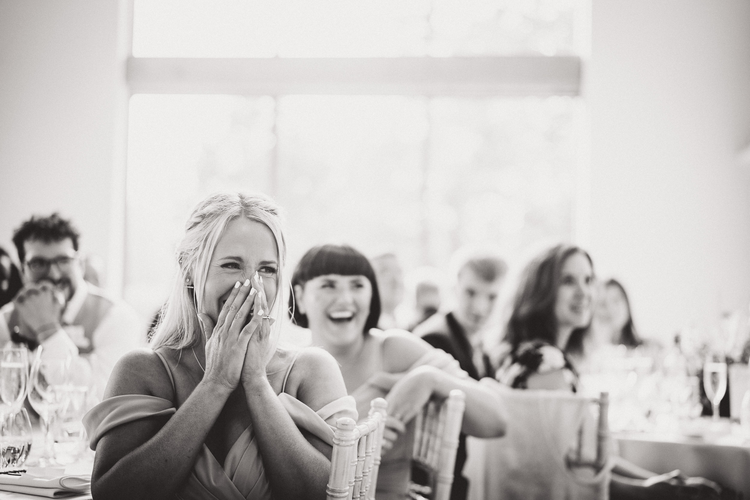 A wedding photographer captures a woman's laughter during a reception.