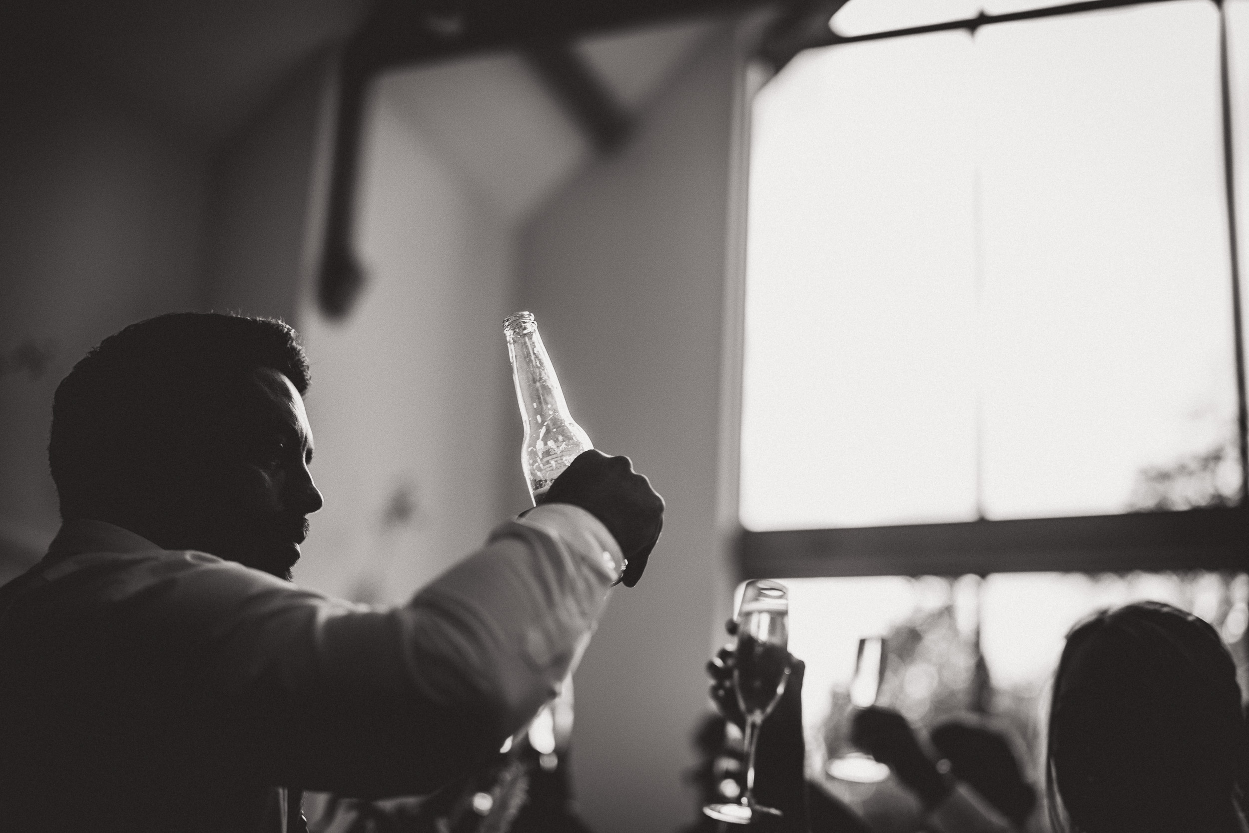 A groom poses with a glass of wine for a wedding photo.