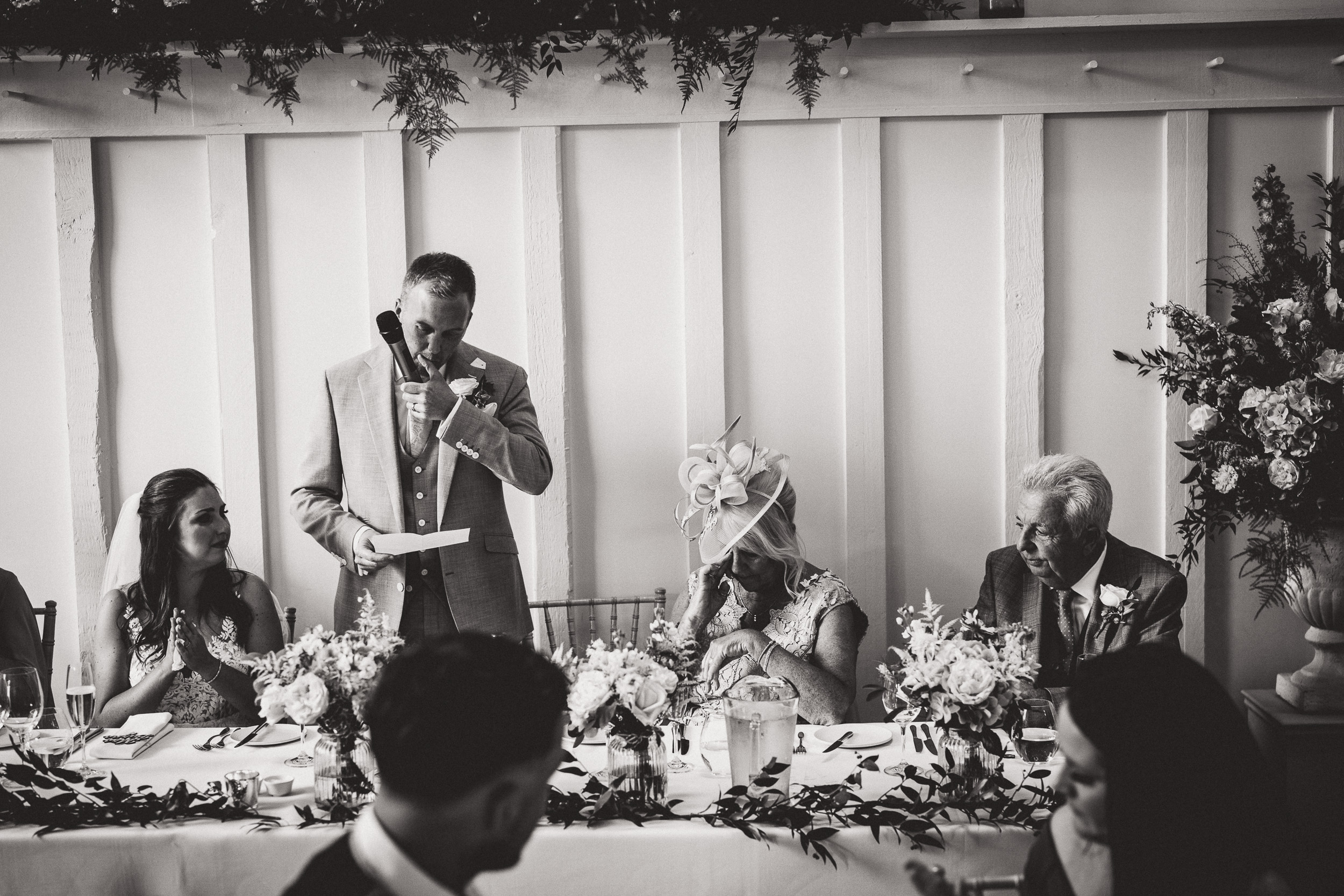 A black and white photo of the groom giving a speech at a wedding.