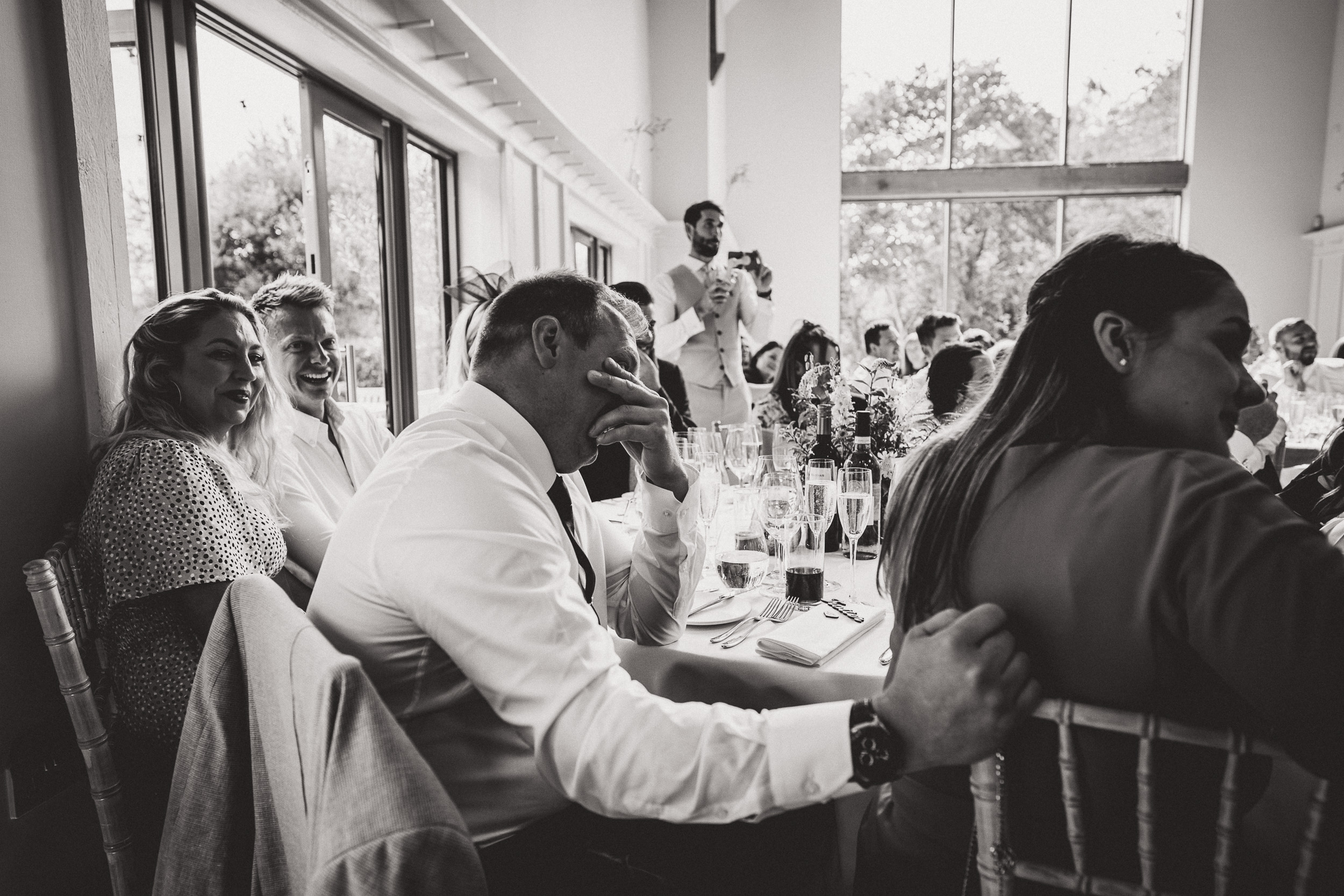 A wedding photographer captures a black and white photo of the groom during the wedding reception.