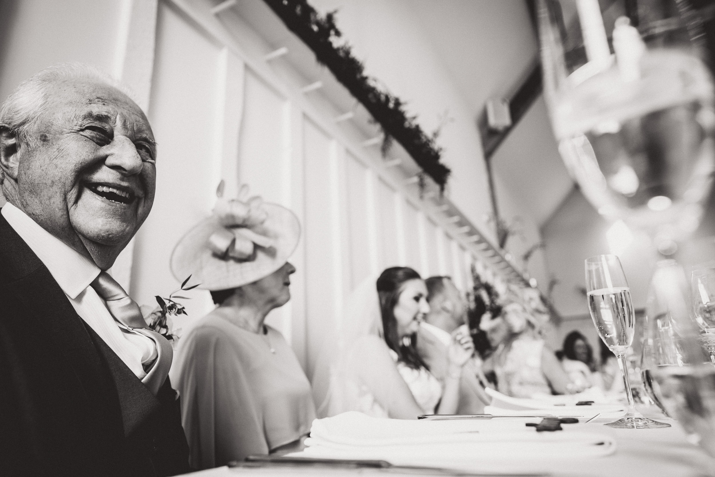 A black and white photo of a groom smiling at a table.