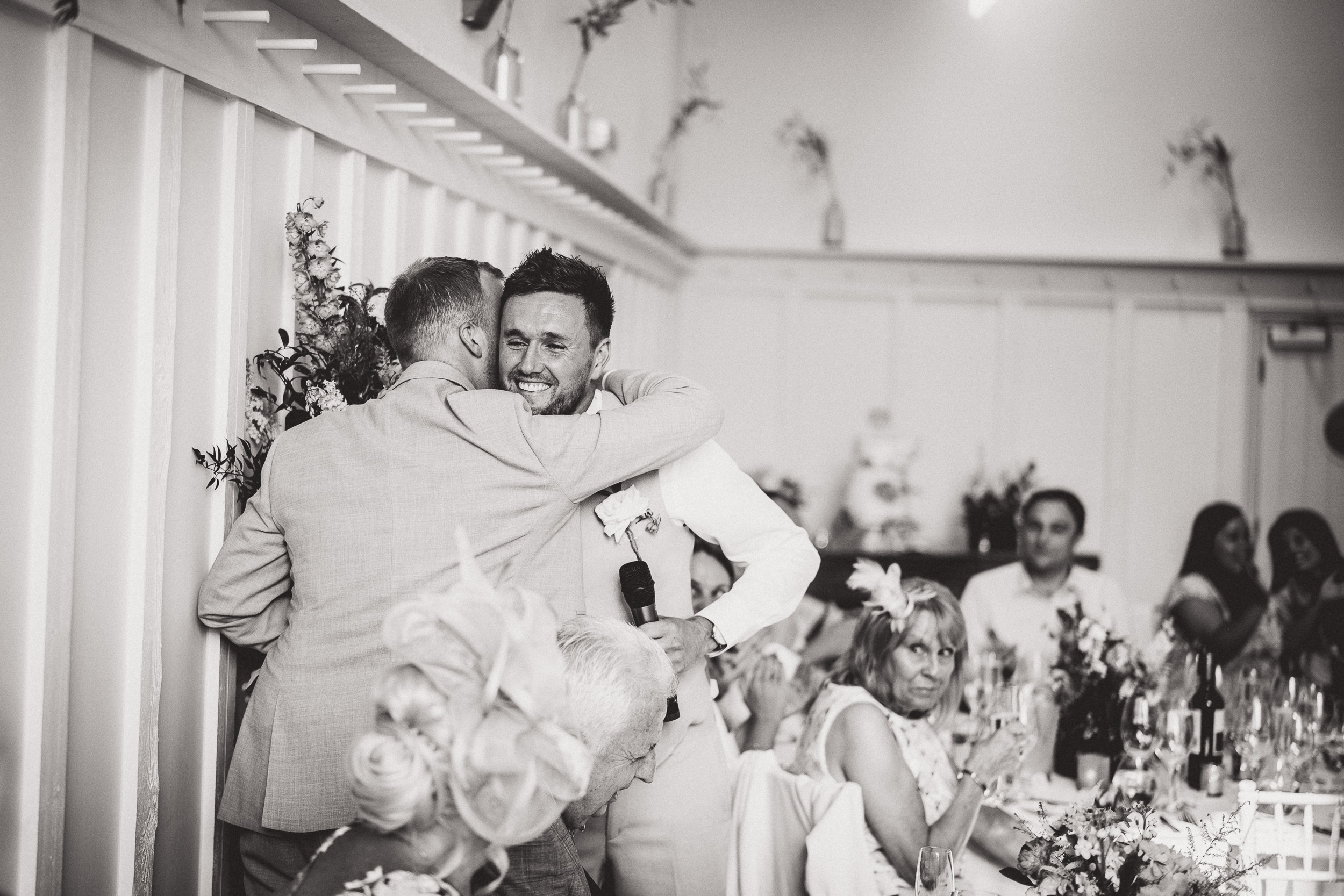 A black and white wedding photo capturing an emotional hug between two men.