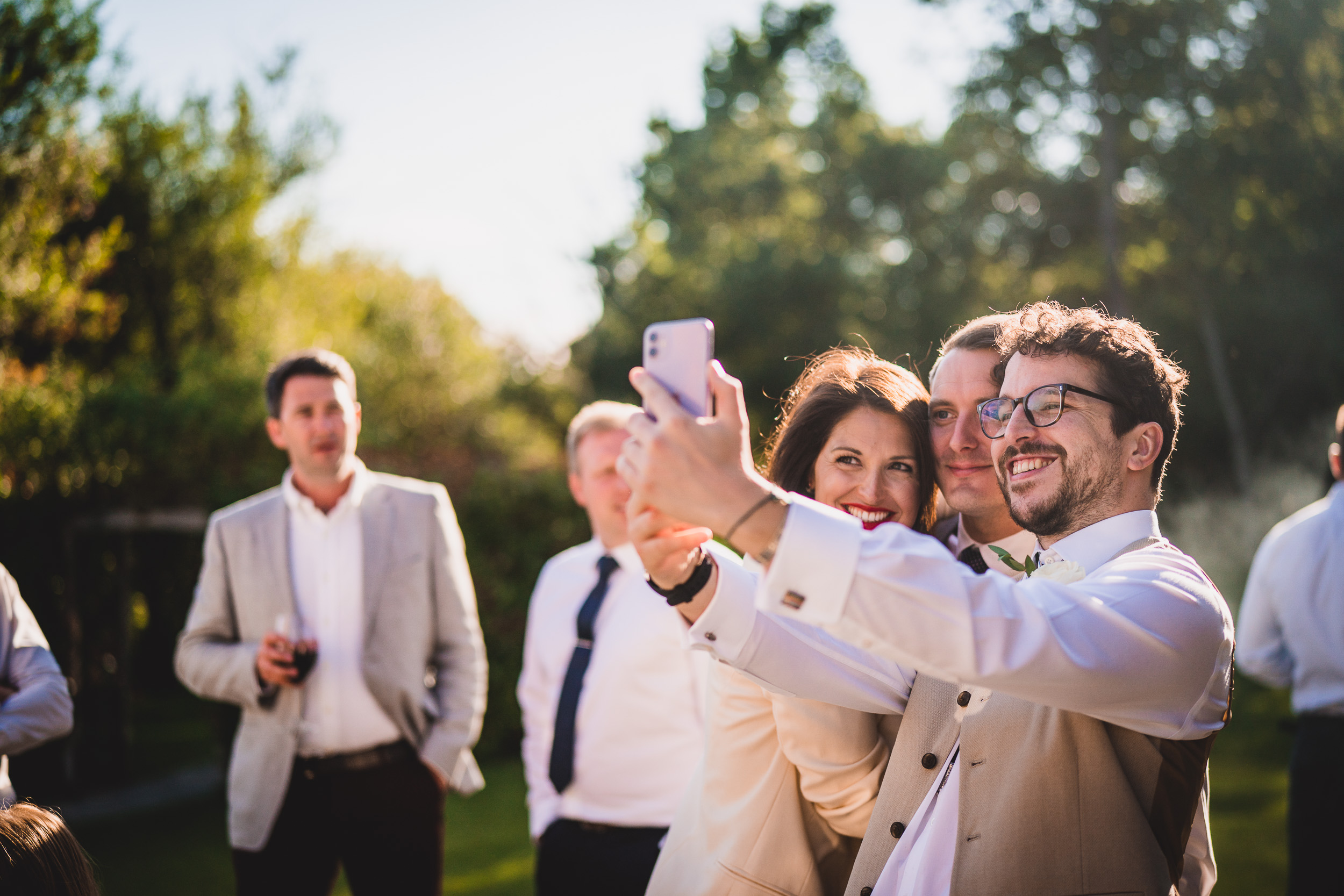 A bride and wedding photographer capturing a group selfie at a wedding.