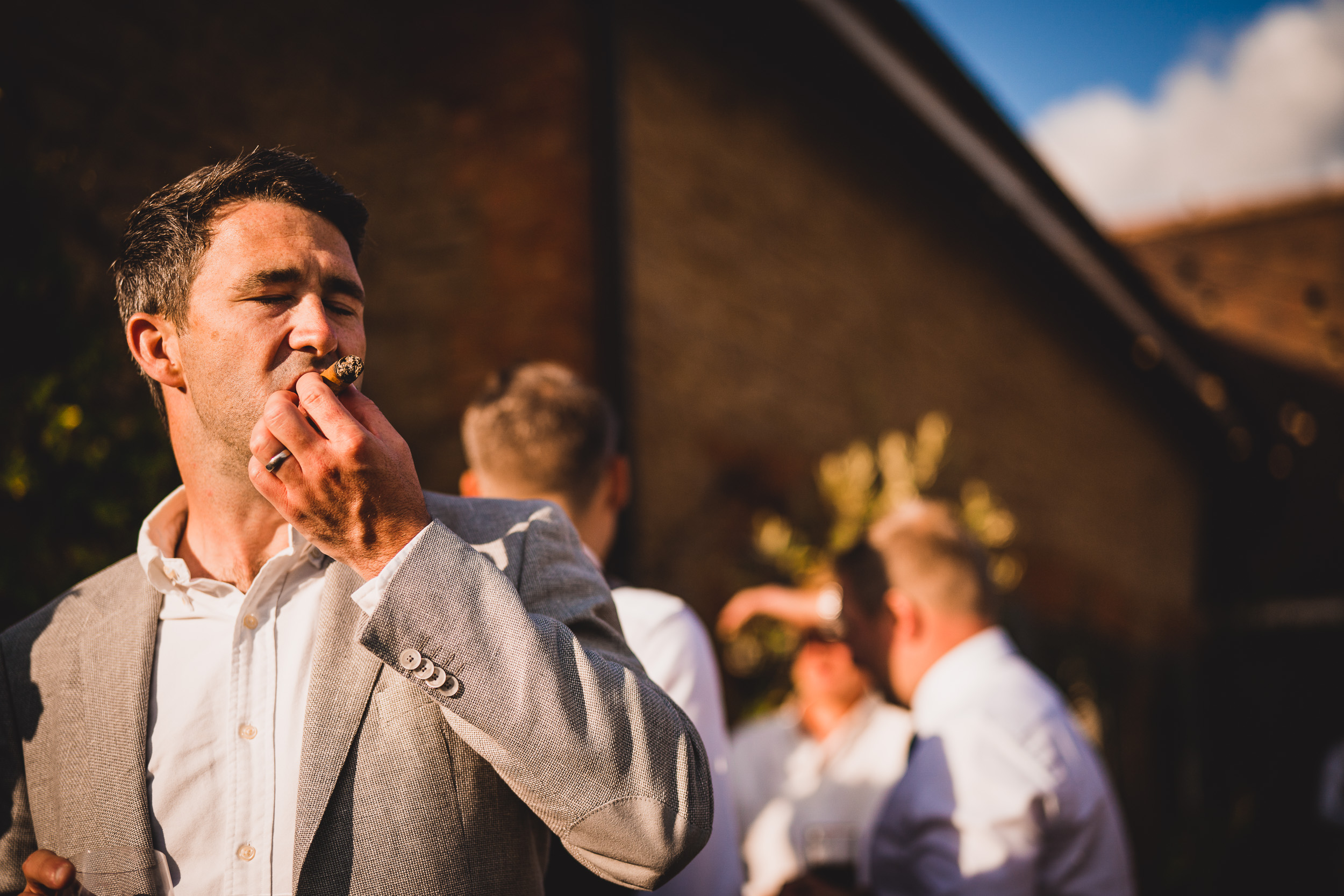 A groom in a suit smoking a cigarette.