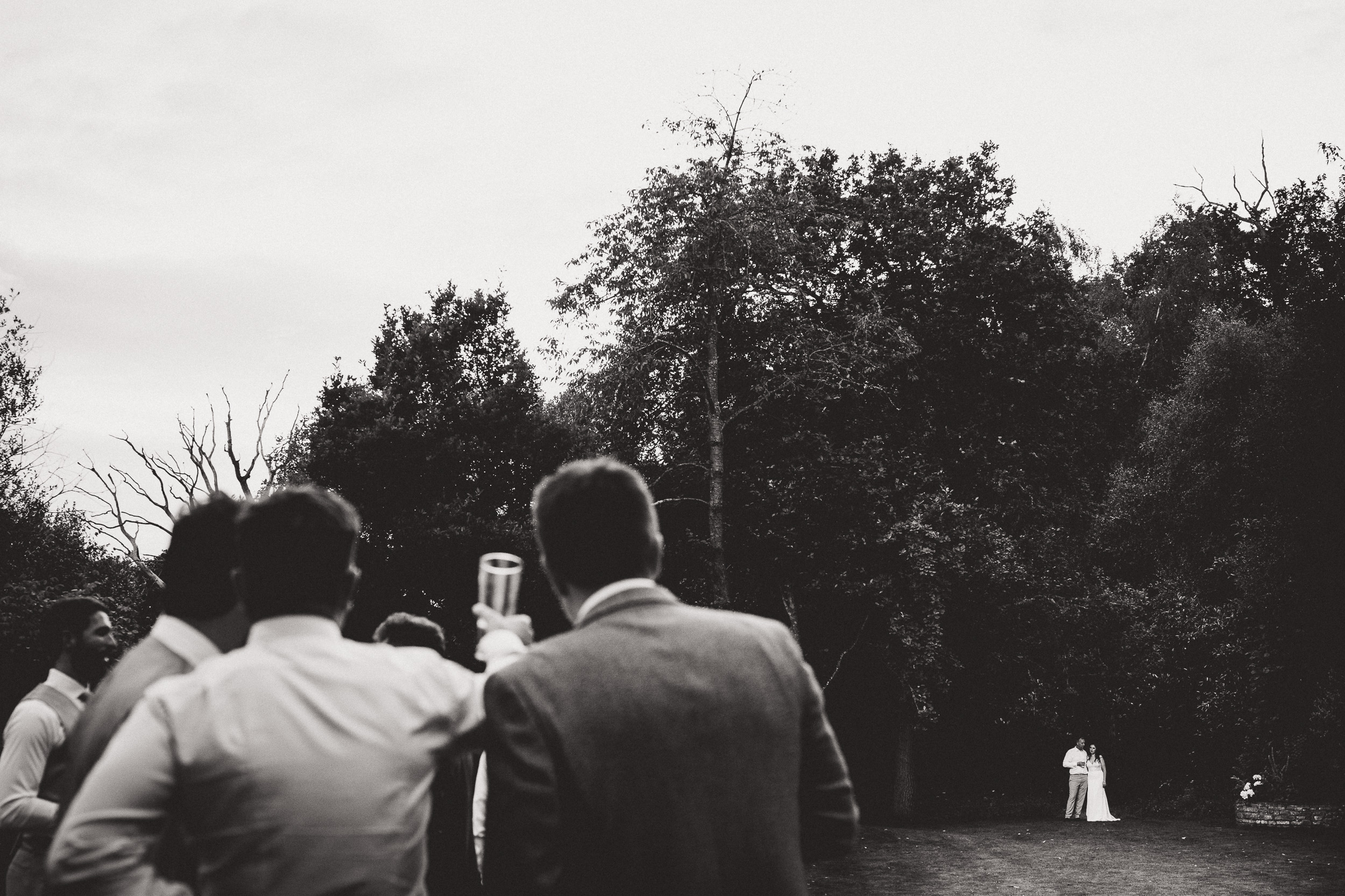 A black and white photo of a wedding party with the bride and groom in the woods, captured by a wedding photographer.