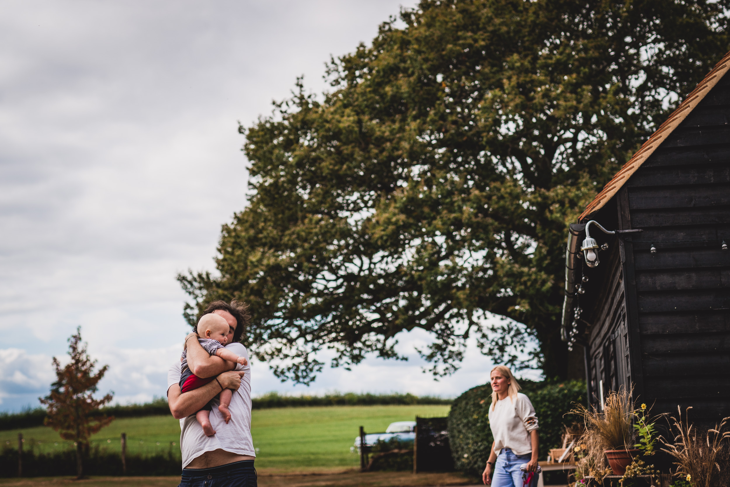 A groom posing with a baby in front of a barn for a wedding photo.