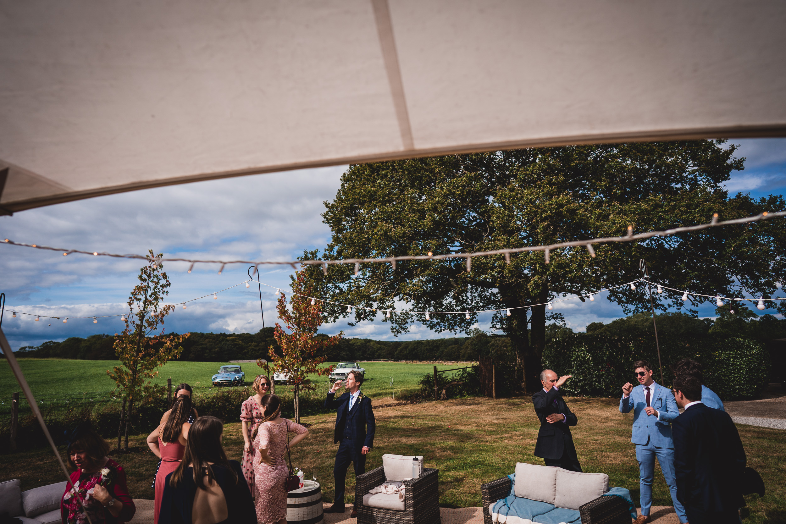 A group of people, including the groom and bride, standing under a tent in a field.