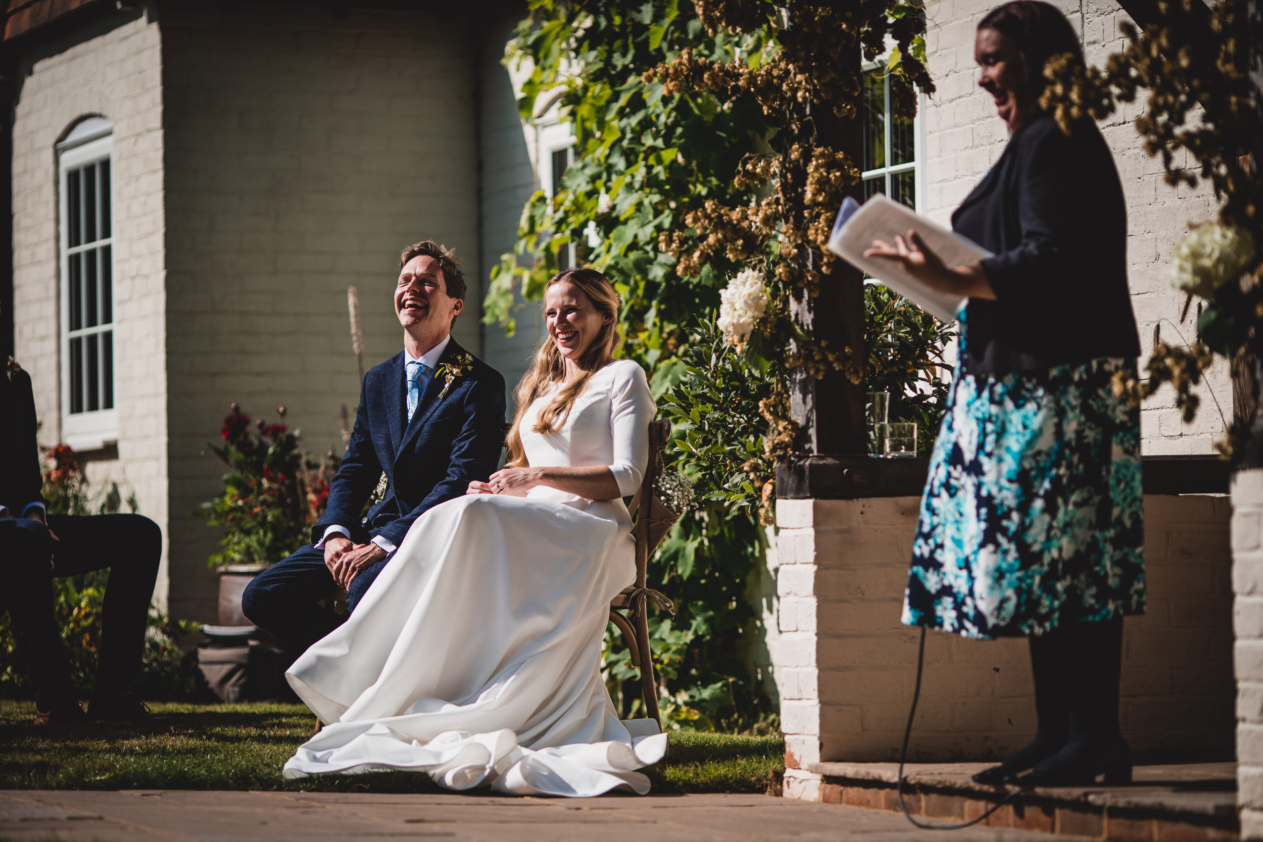 A wedding photo capturing the bride and groom sitting on a bench in front of a house.