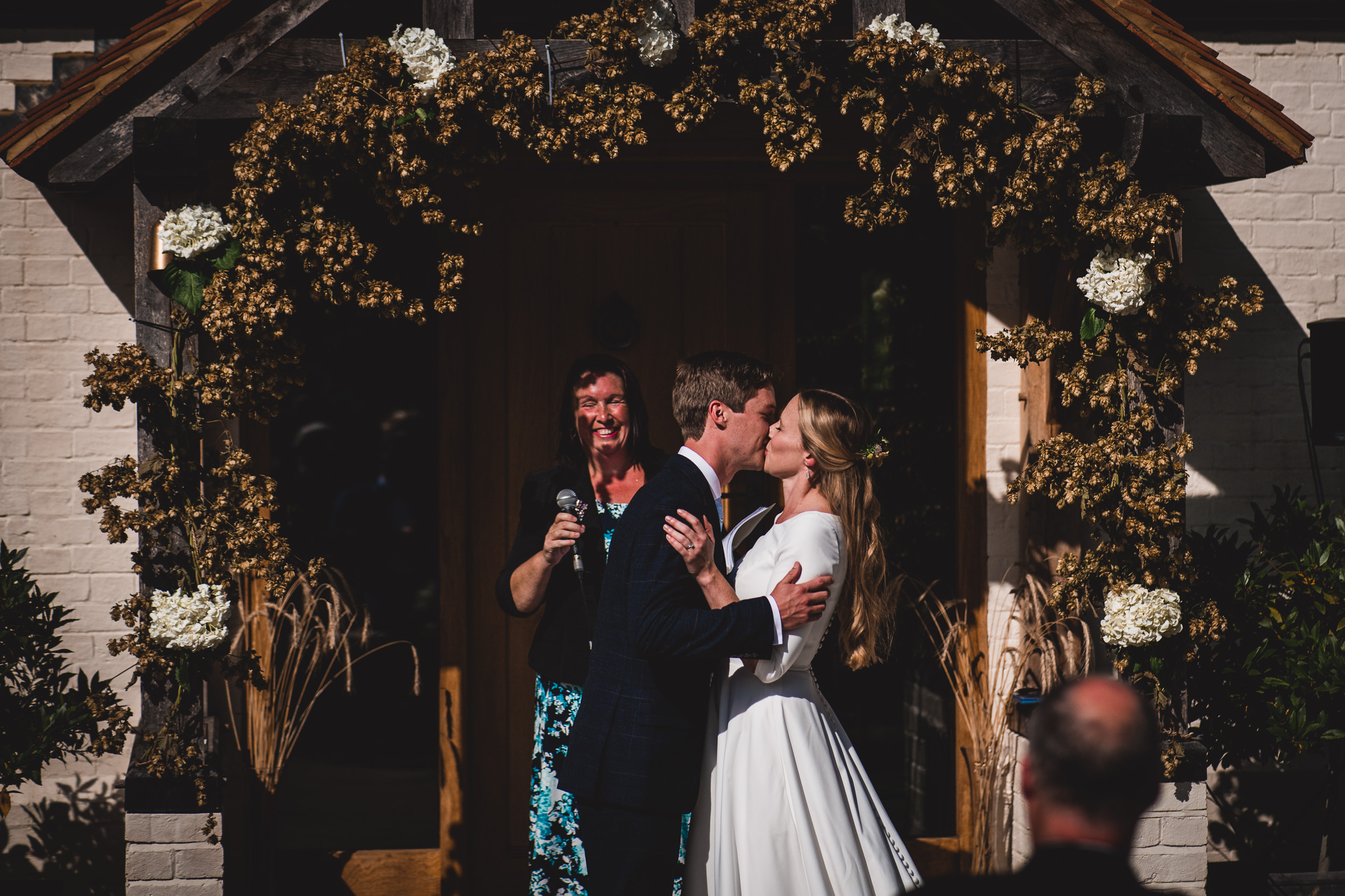 A groom and bride share a kiss at their wedding in front of a house.