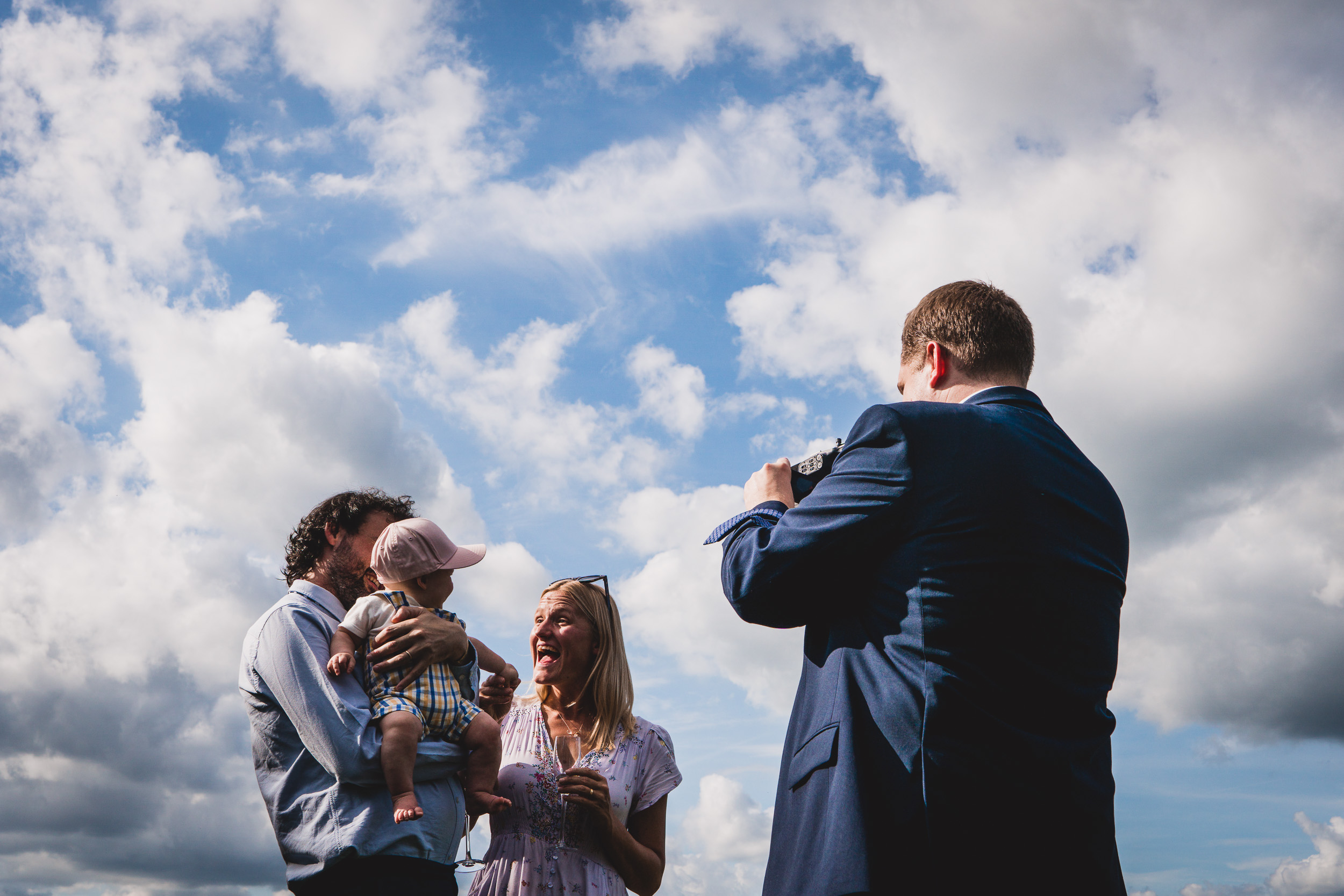 A groom is taking a wedding photo of a bride and a baby.