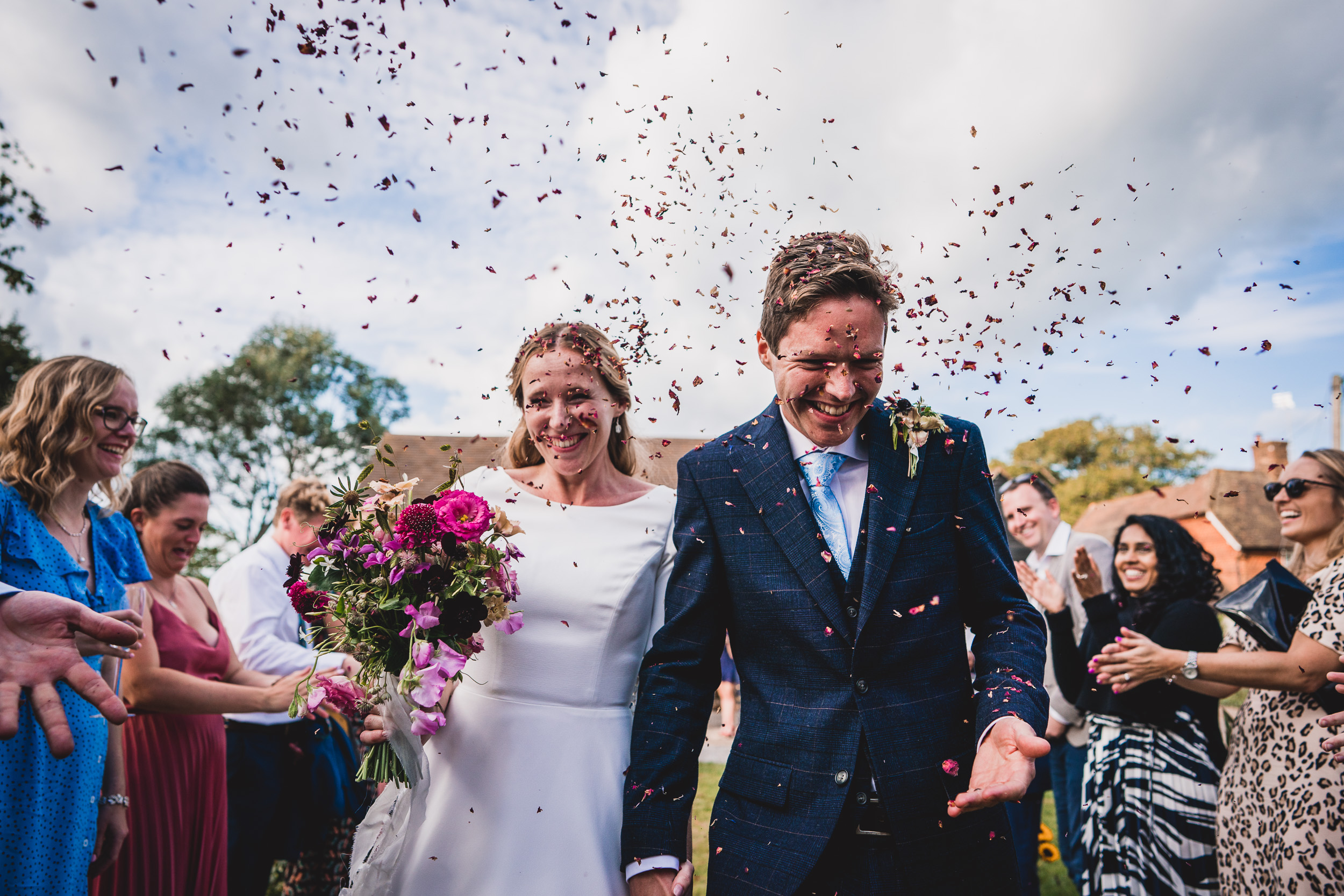 A groom and bride walk down the aisle with confetti, captured by a wedding photographer.