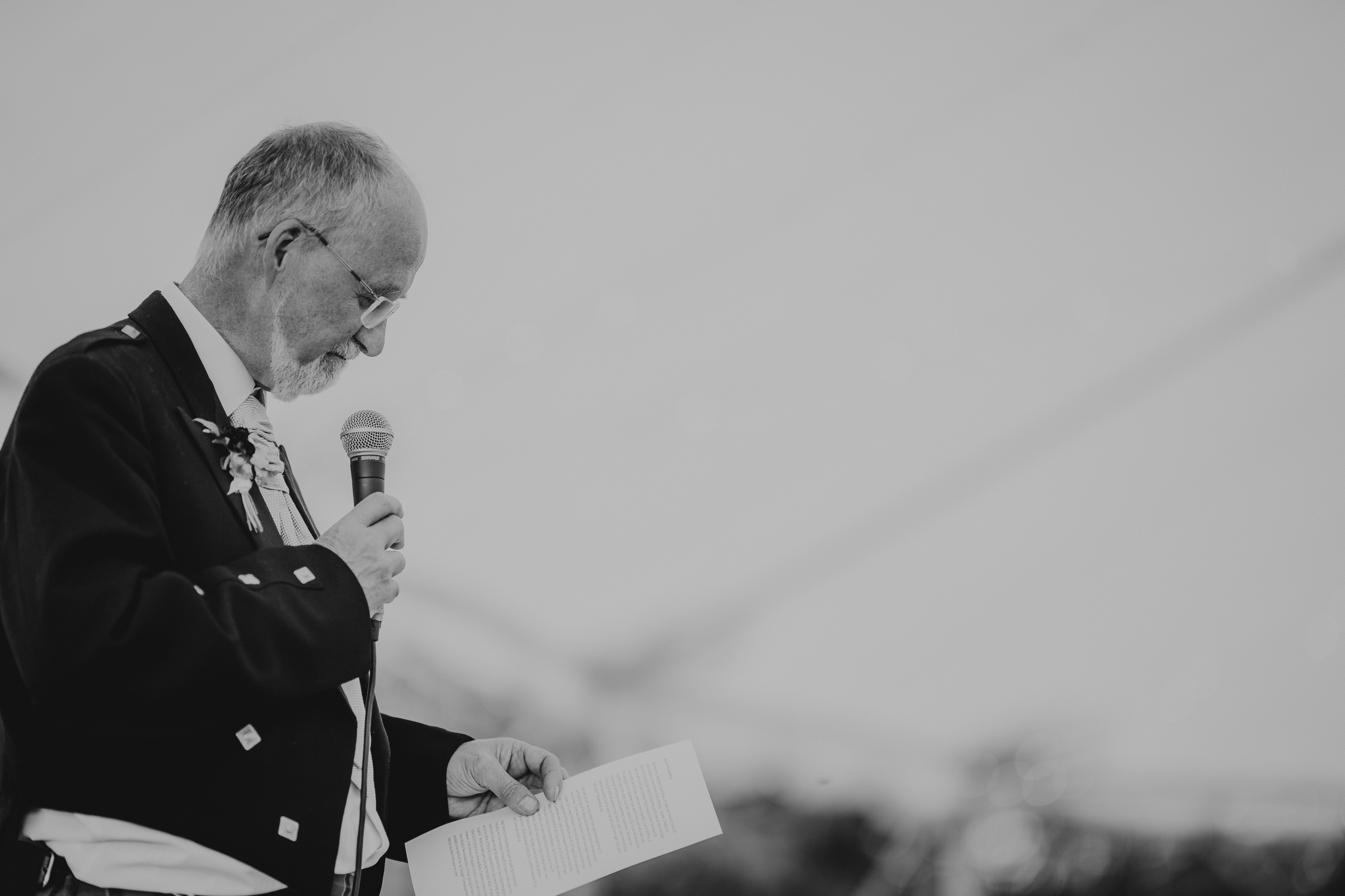 A wedding photographer capturing the bride in her wedding photo, while a man in a kilt speaks into a microphone.