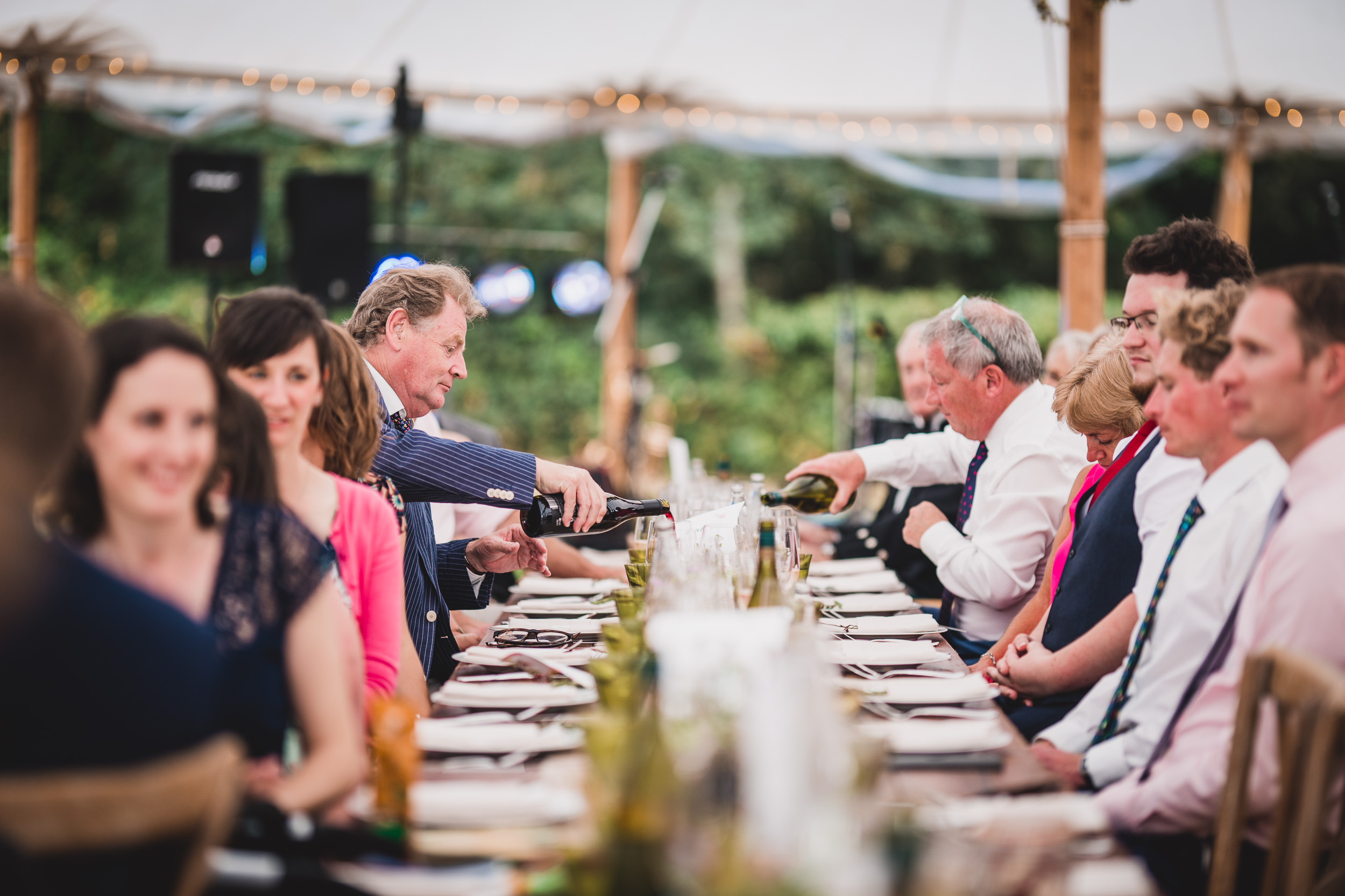 A group of people, including the groom, sitting at a long table for a wedding photo.