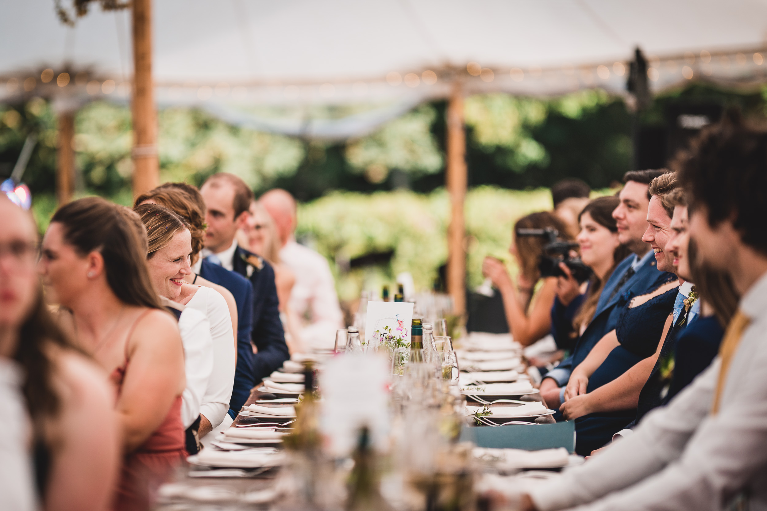 A wedding photographer capturing the bride and guests seated at a reception table.