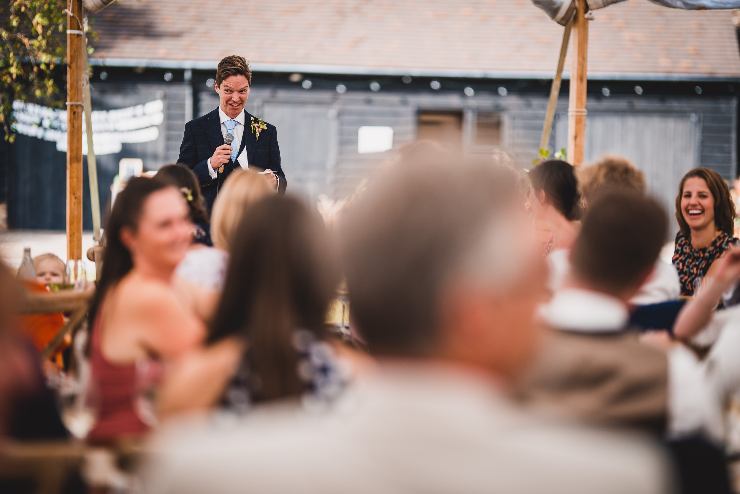 A man giving a speech at an outdoor wedding captured by the wedding photographer.