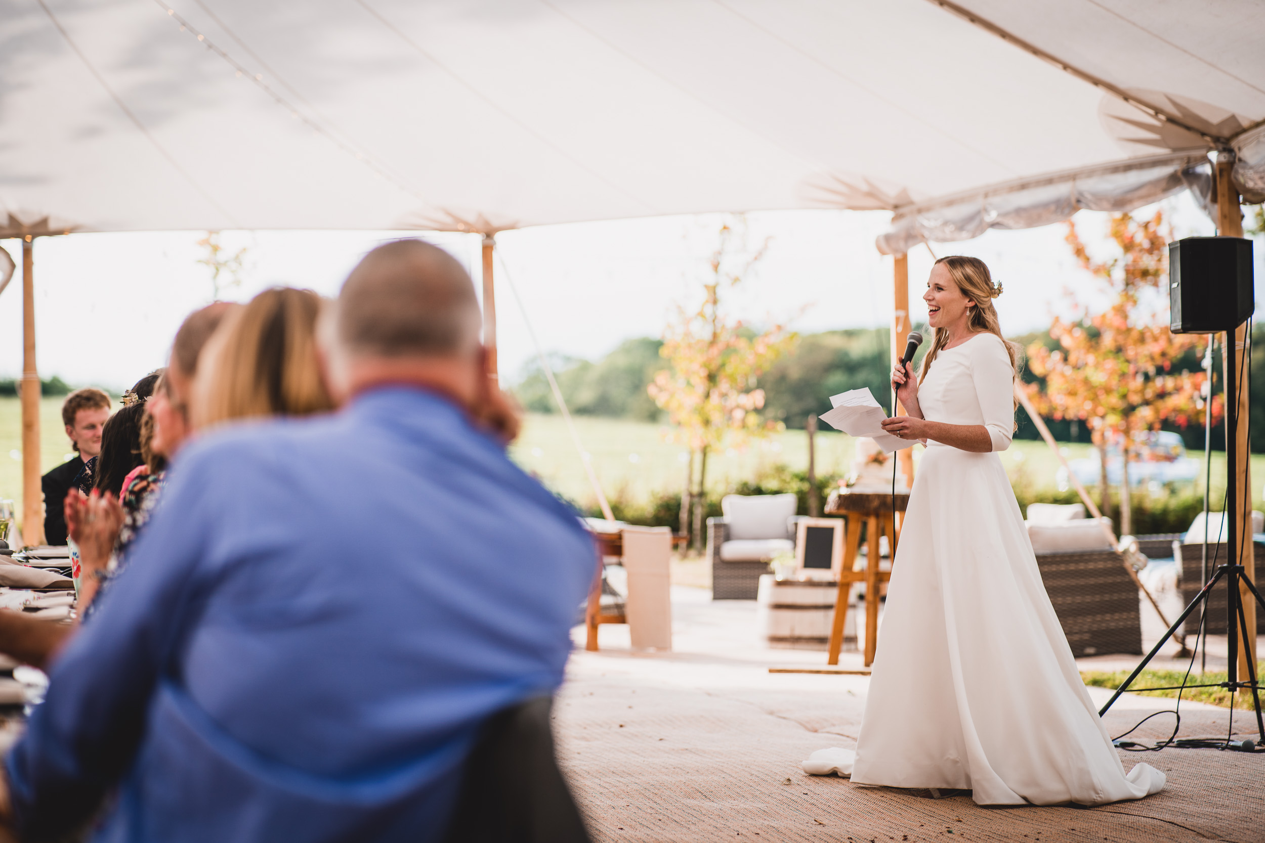 A bride captured by the wedding photographer while giving a speech at an outdoor wedding.