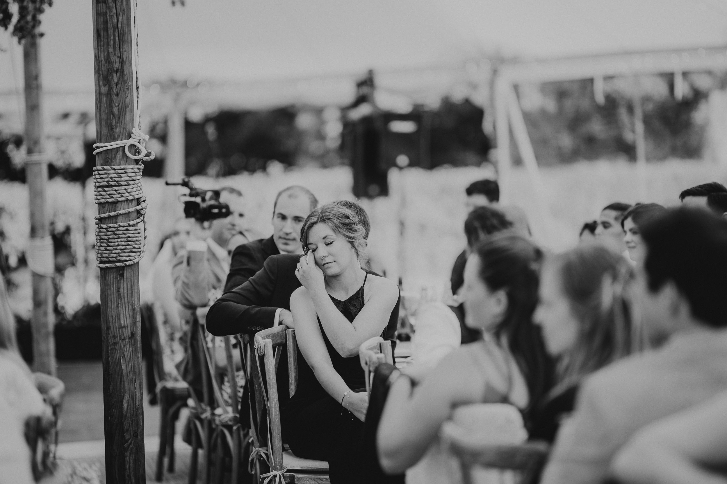 A bride is sitting in a chair at a wedding ceremony while being photographed by the wedding photographer.