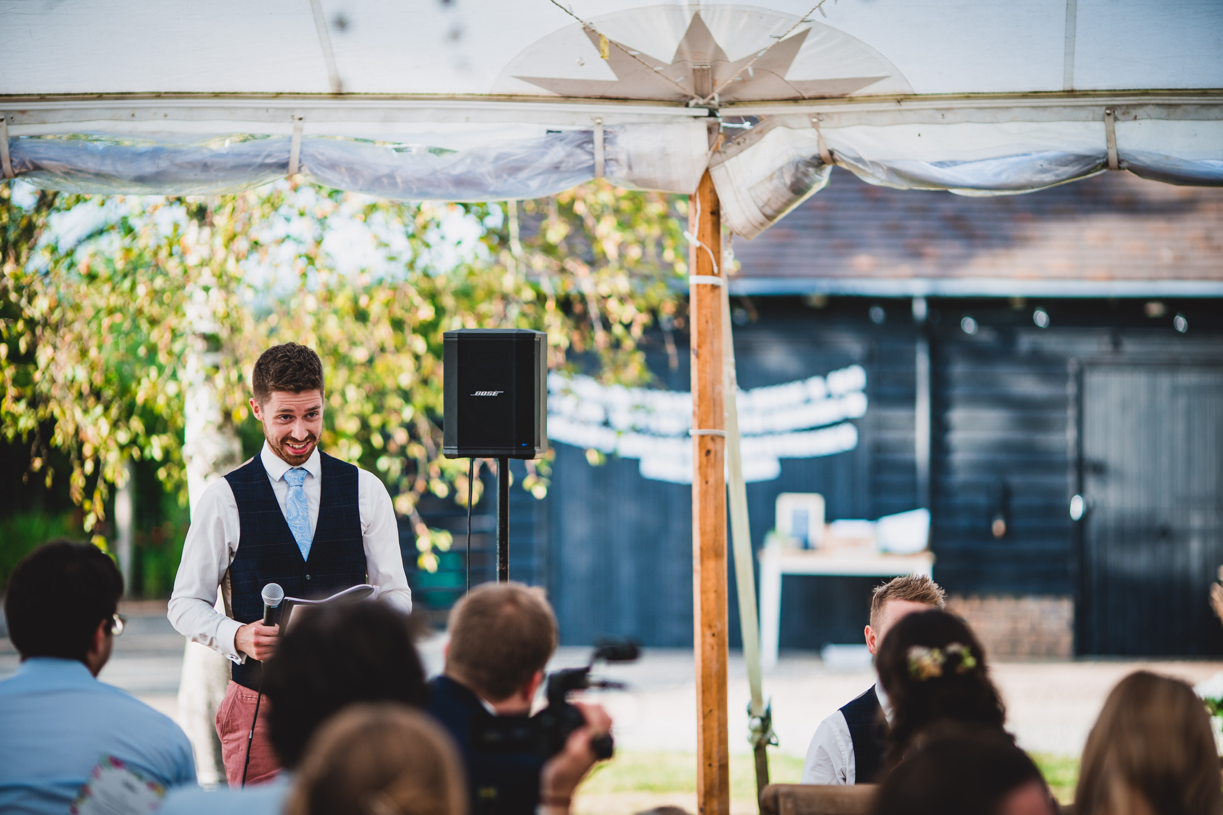 A man giving a speech at an outdoor wedding reception.