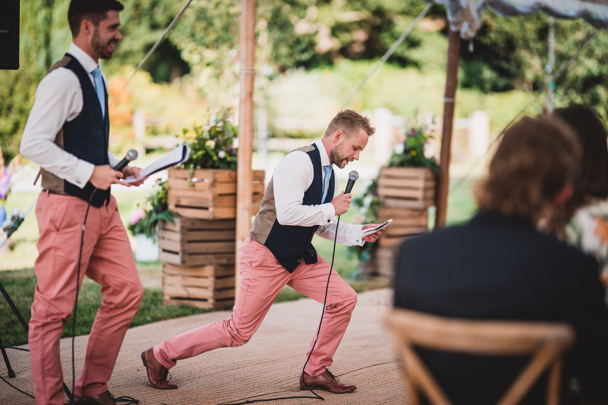 A wedding photographer captures a man in pink pants holding a microphone at the bride's wedding.