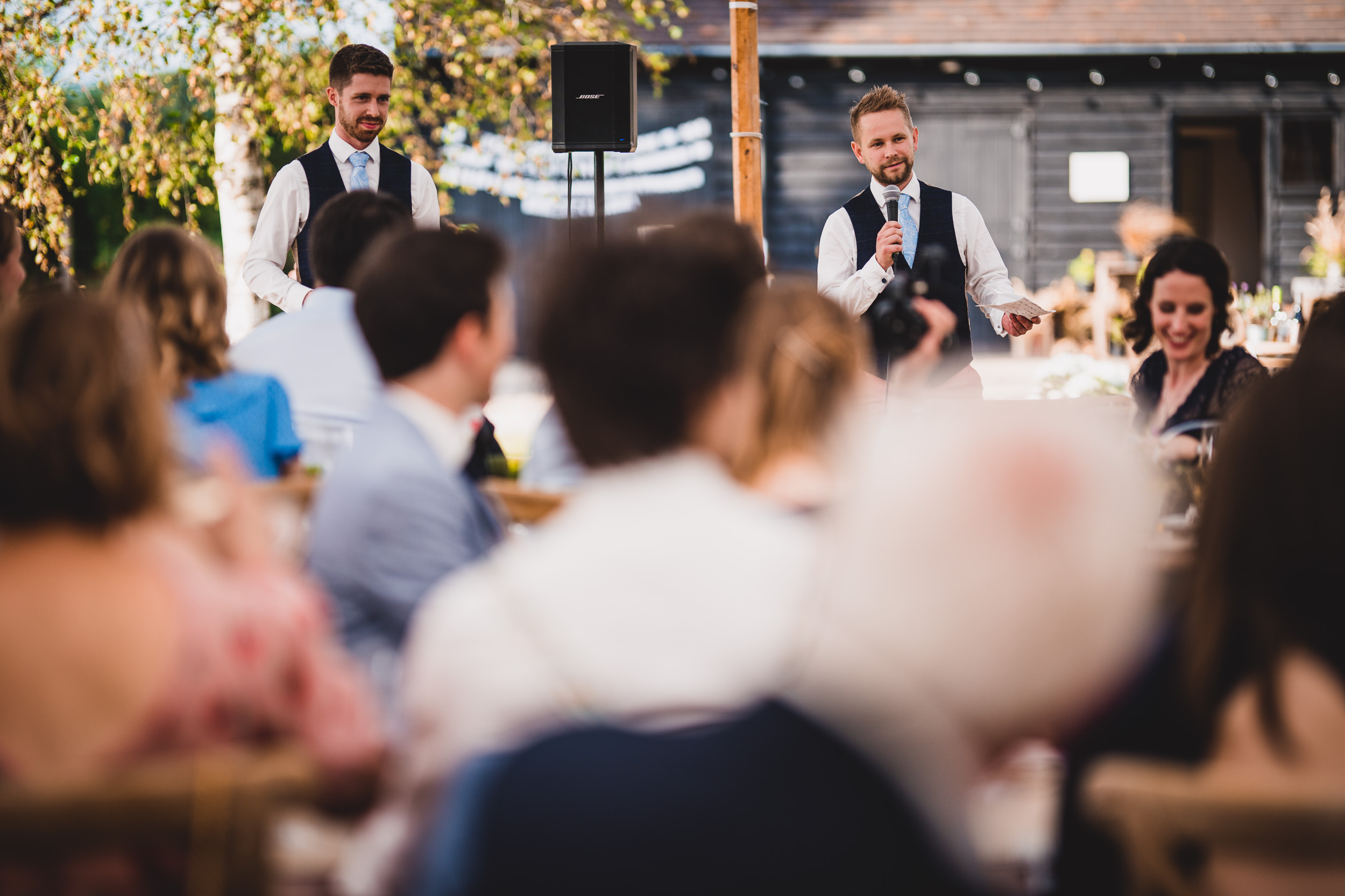 The groom is addressing the wedding party during the outdoor ceremony.